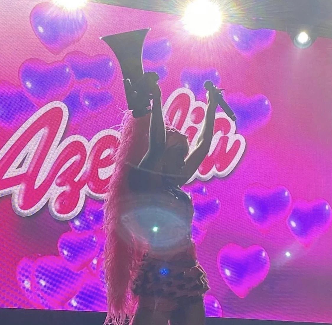 Performer with a pink backdrop featuring heart shapes, holding a megaphone and microphone, with "Azealia" text in the background.