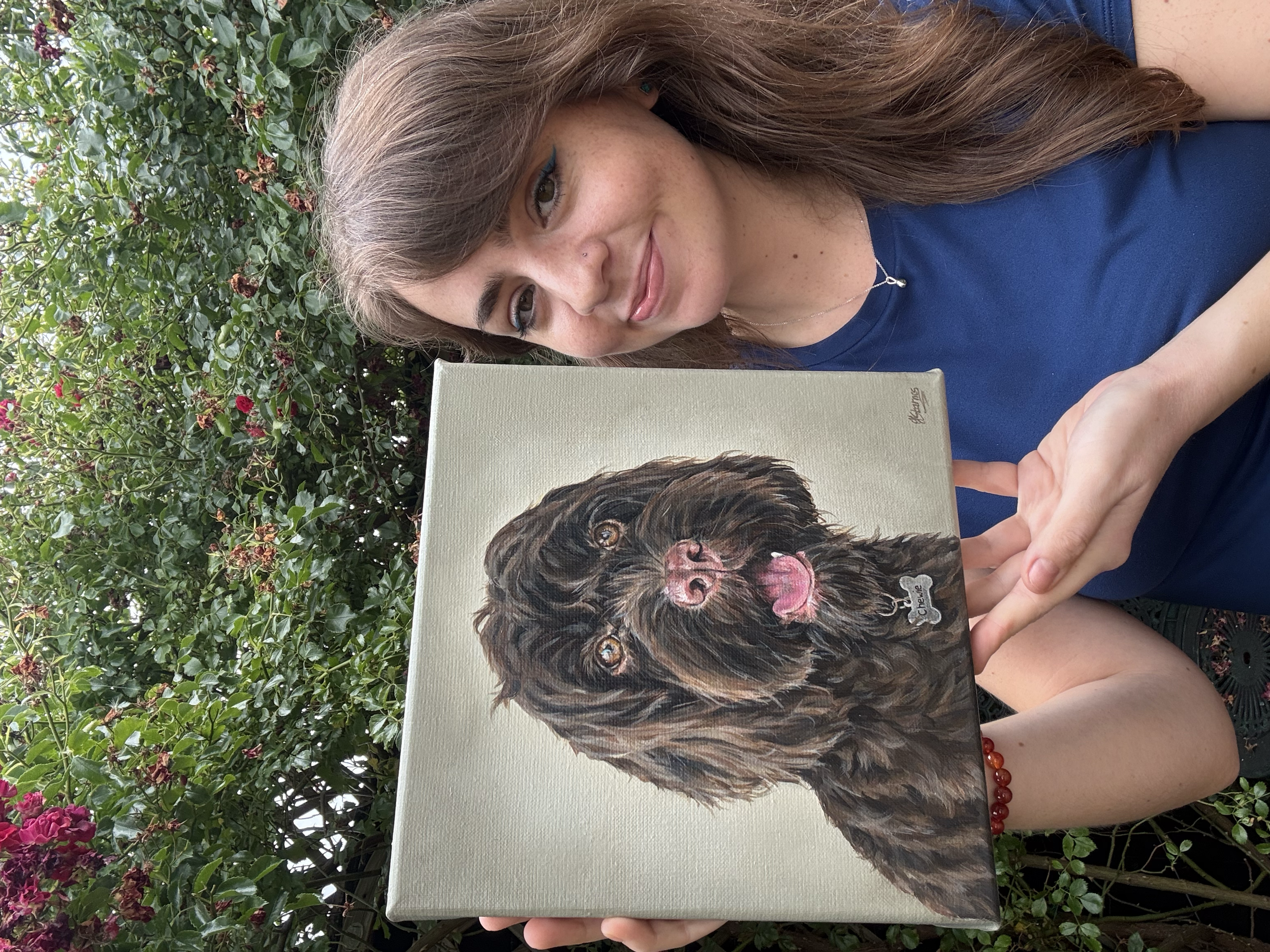 artist holds up a portrait painting of a chocolate brown cockapoo dog. 