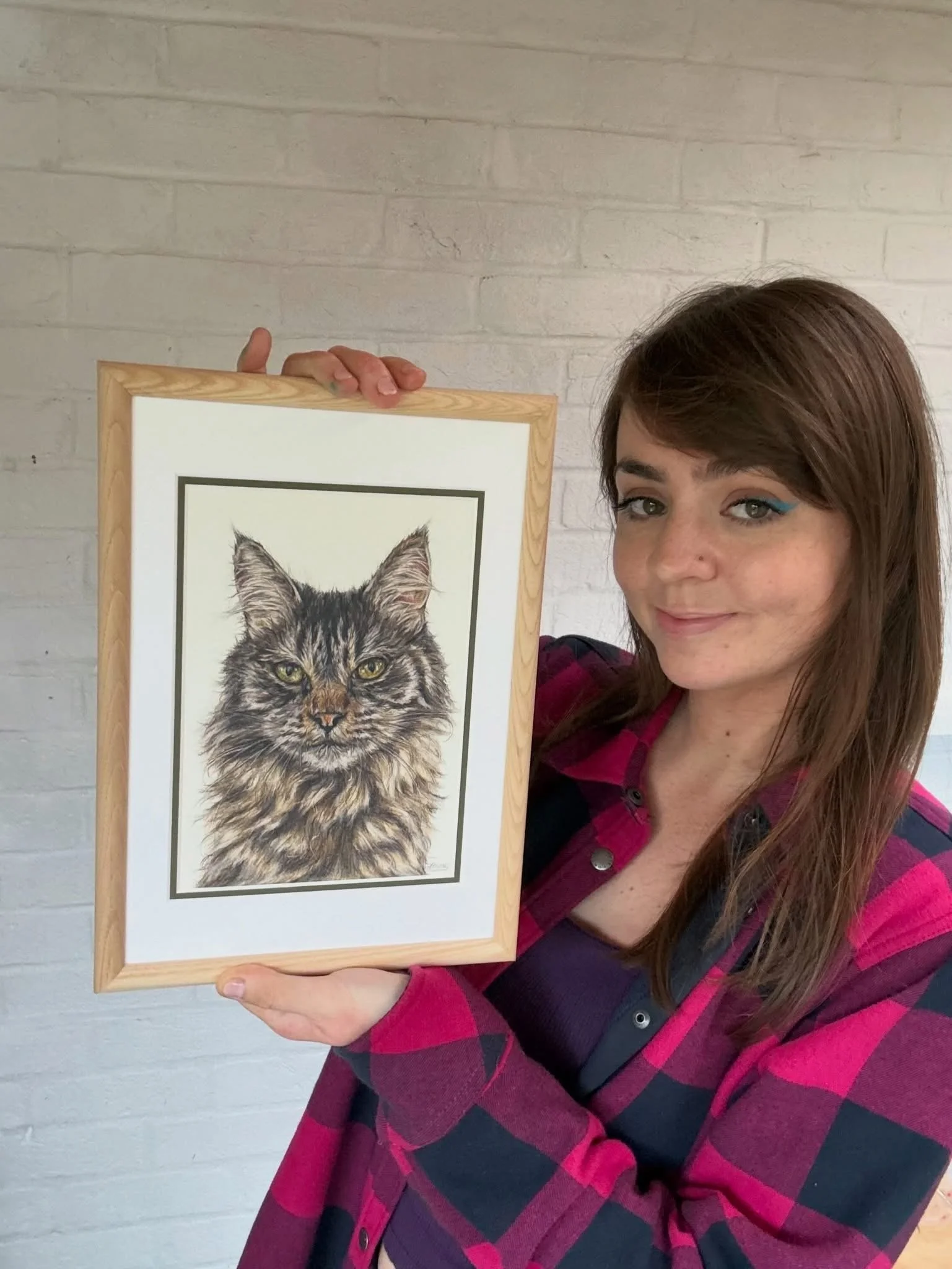 artist holds a coloured pencil drawing of a Maine coon cat. 