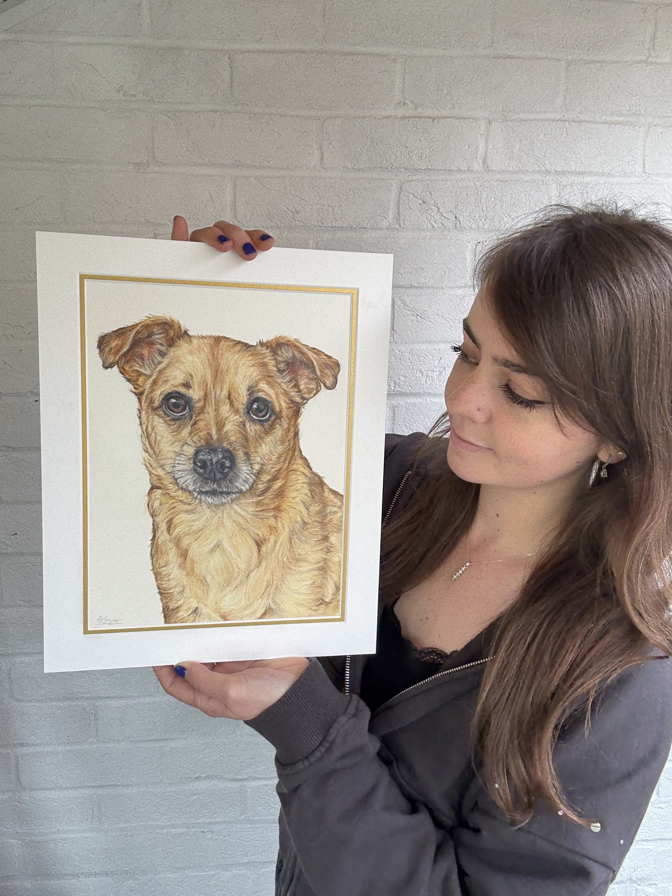 artist holds a detailed coloured pencil drawing of a light brown dog.