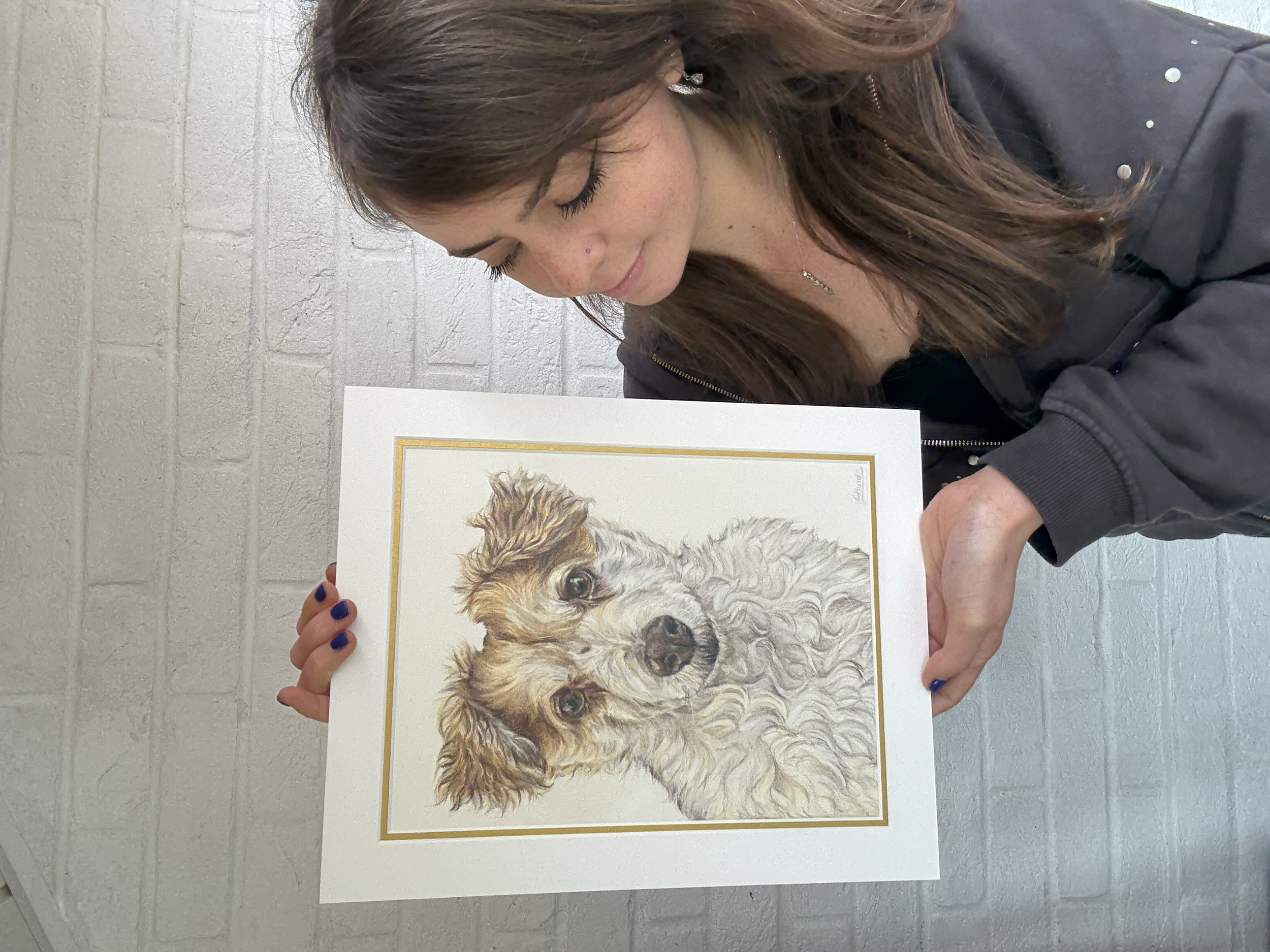 artist holds a detailed coloured pencil drawing of a white and cream dog.