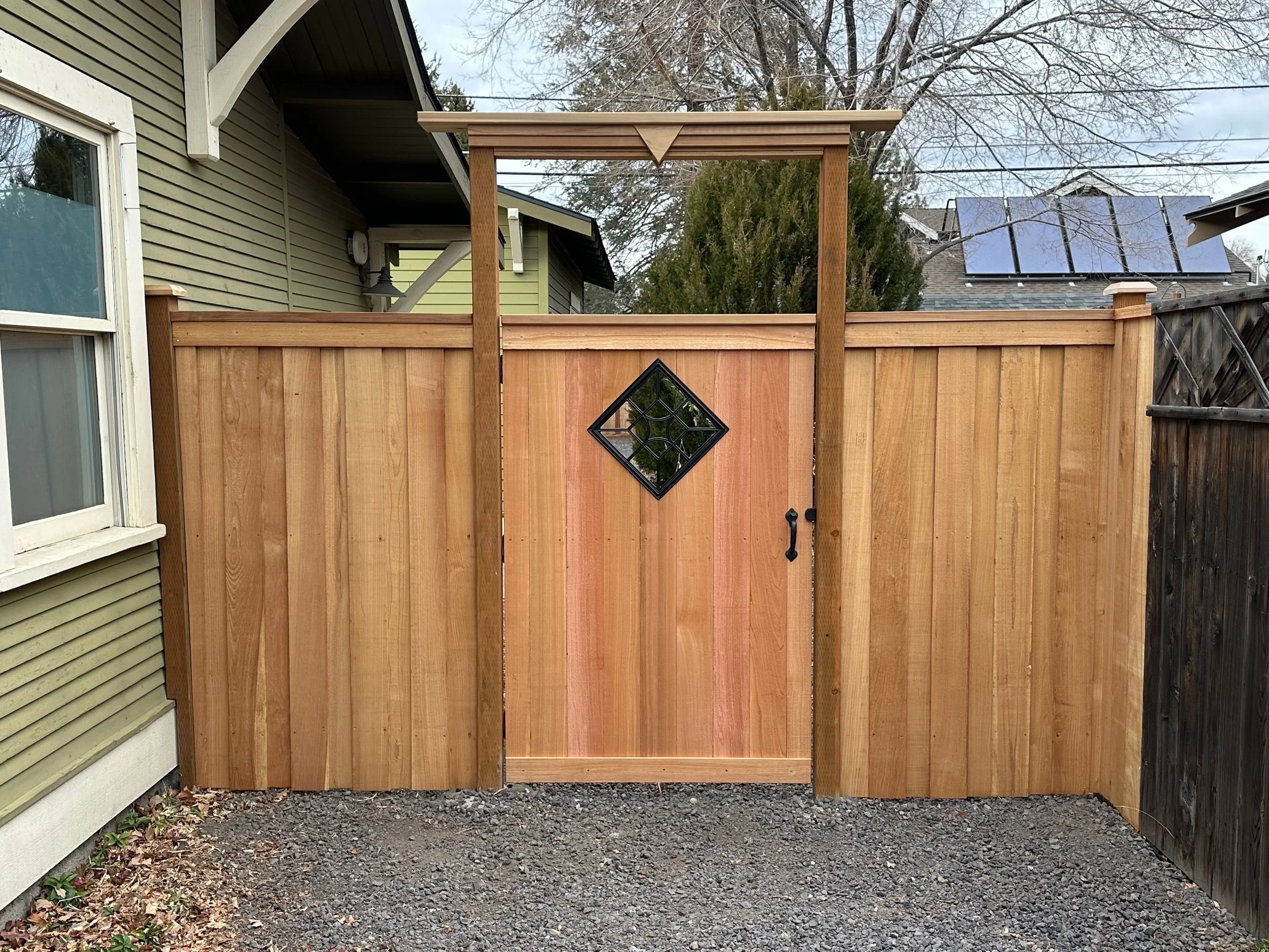 Wooden backyard gate and fencing with a small door featuring a diamond-shaped window