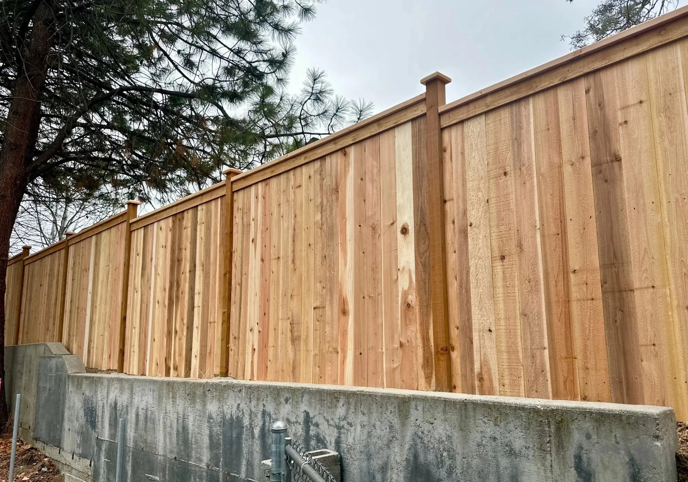 New wooden fence installed on a concrete foundation with trees in the background.