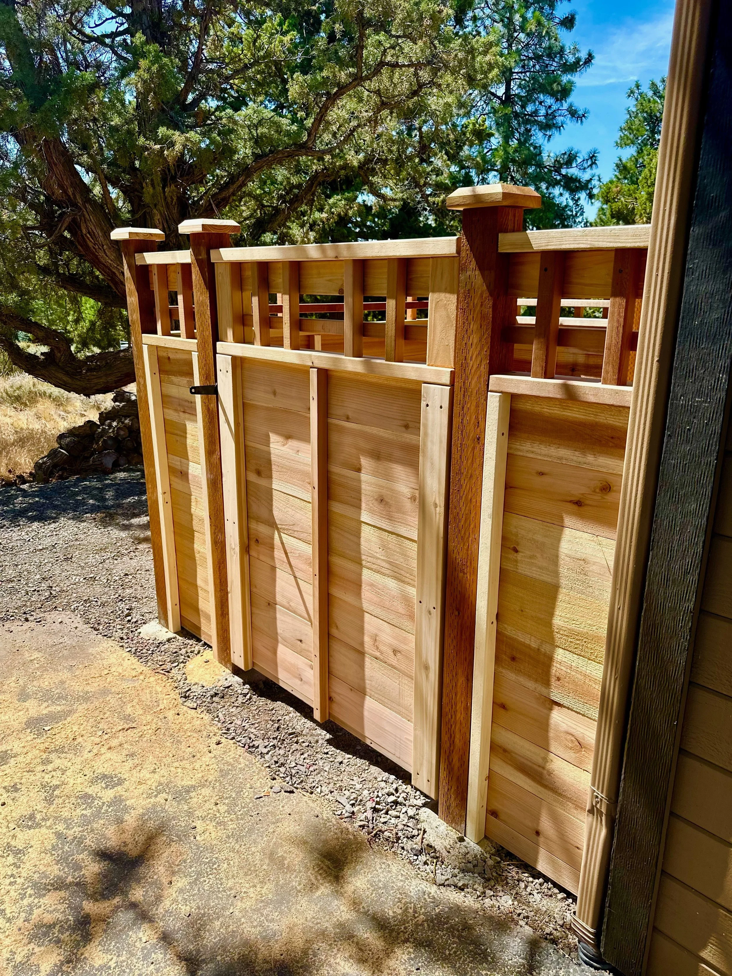 Wooden gate and fence outside near a tree with green foliage and a blue sky.