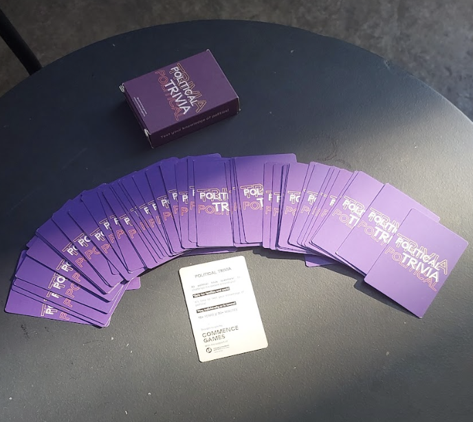 A purple deck of cards labeled 'Arizona Political Trivia' spread out on a black table with a separate white card titled 'Political Trivia' and a purple box.