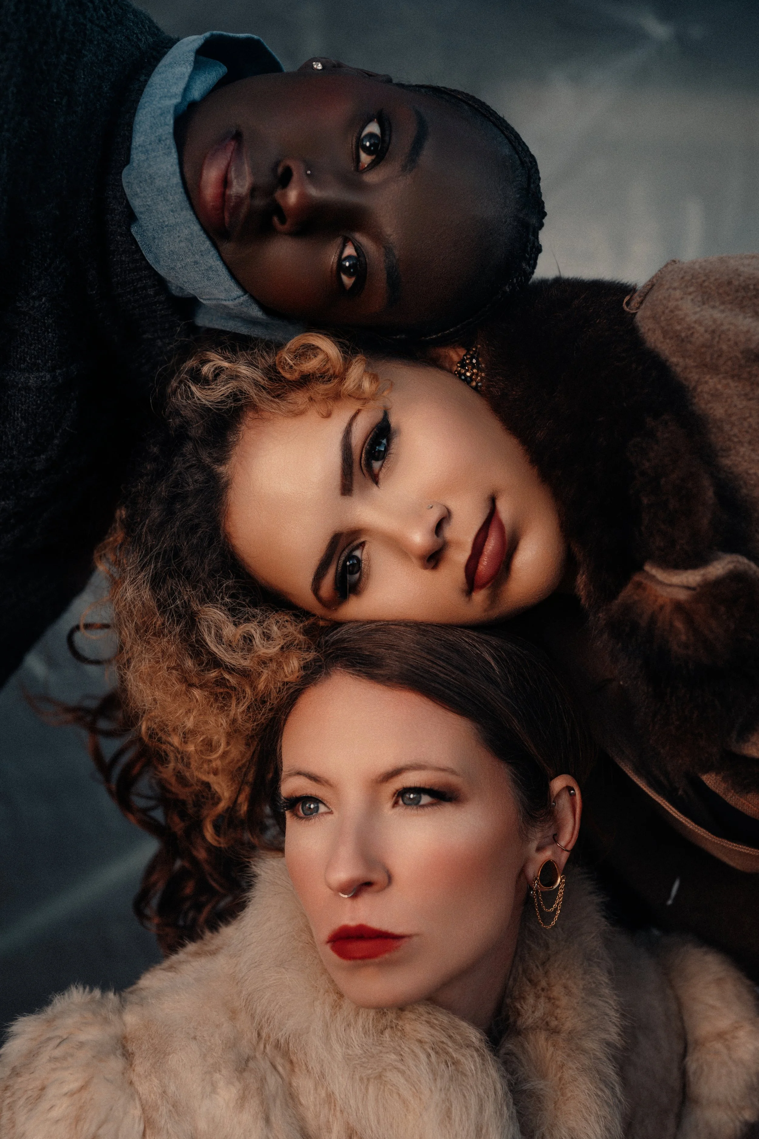 Three women lying on the ground with their heads close together, looking up at the camera.