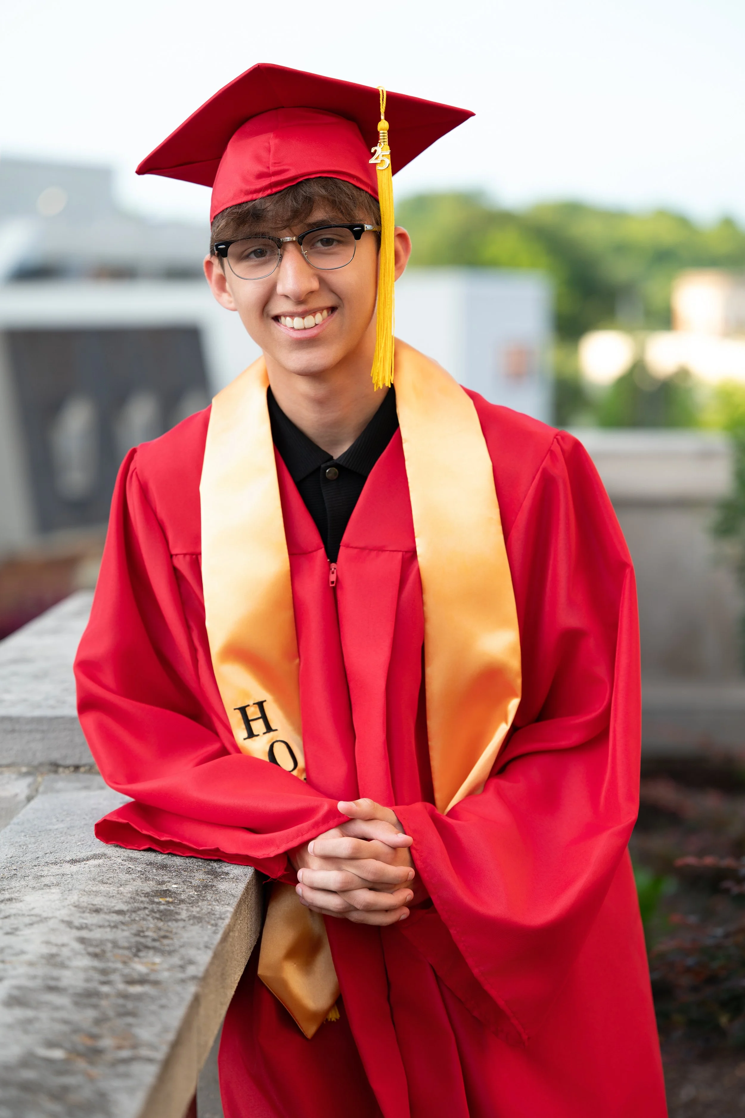 High school senior in red cap and gown smiling during graduation portrait session.