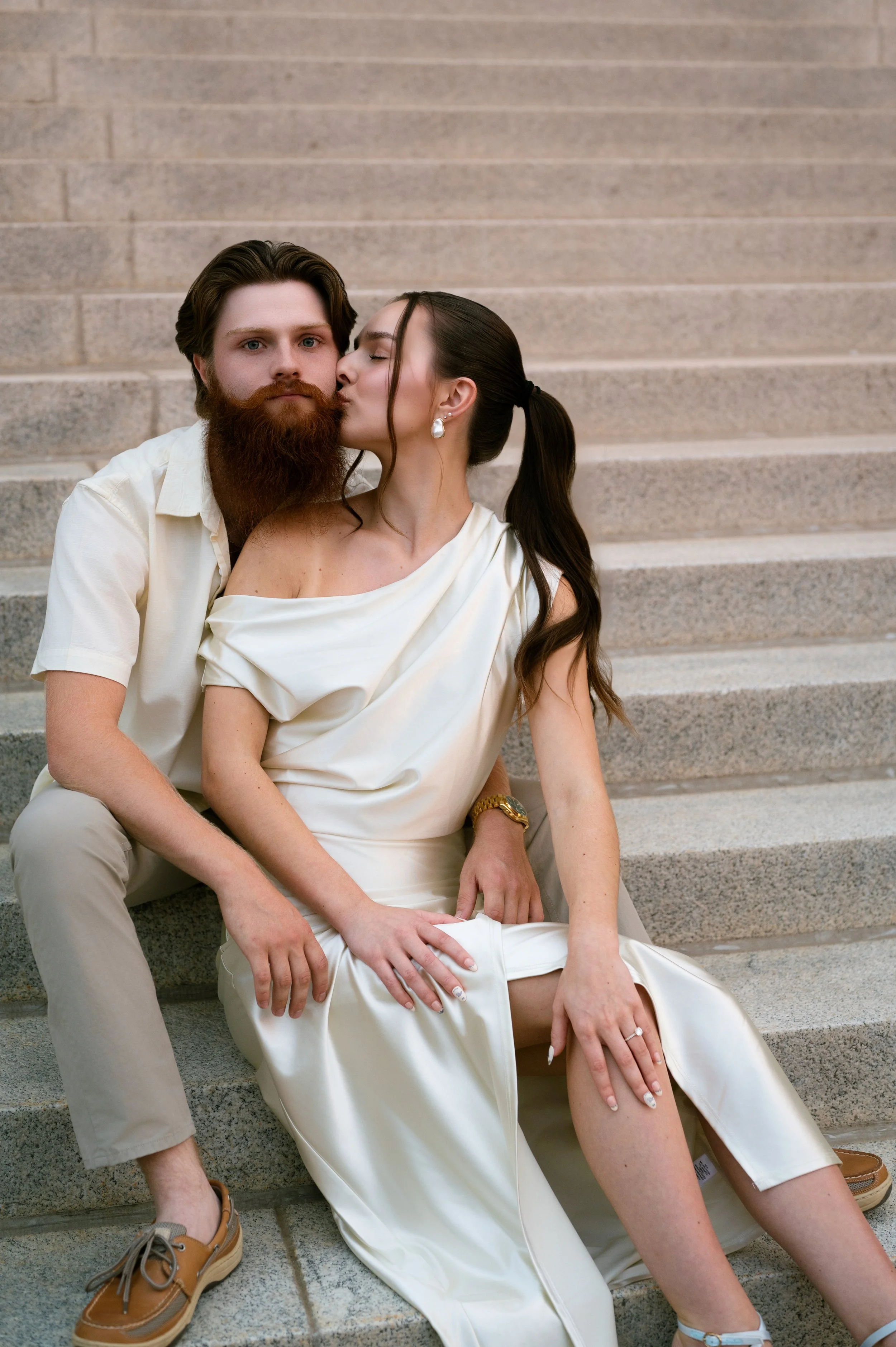 A man and woman sitting on stairs, with the woman kissing the man's cheek.