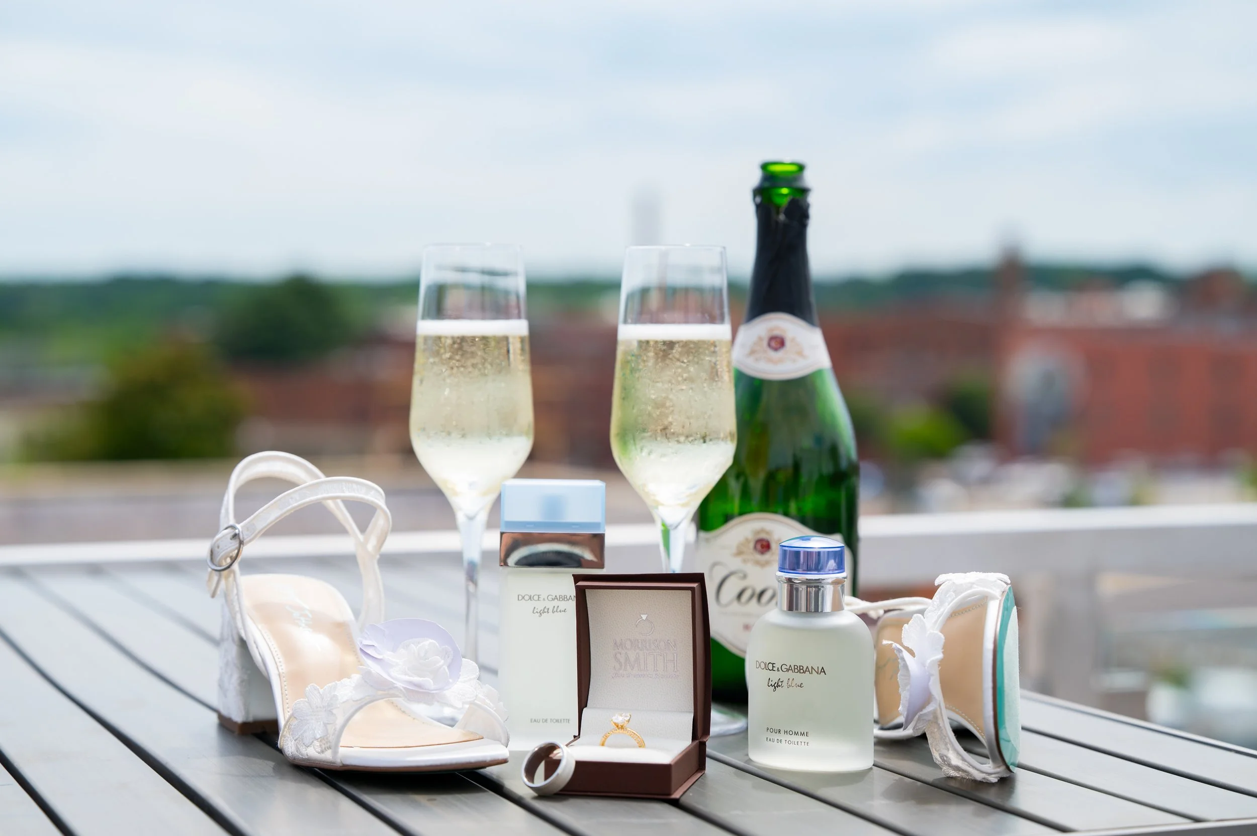 Champagne bottles, two flute glasses filled with champagne, white bridal shoes with floral embellishments wedding