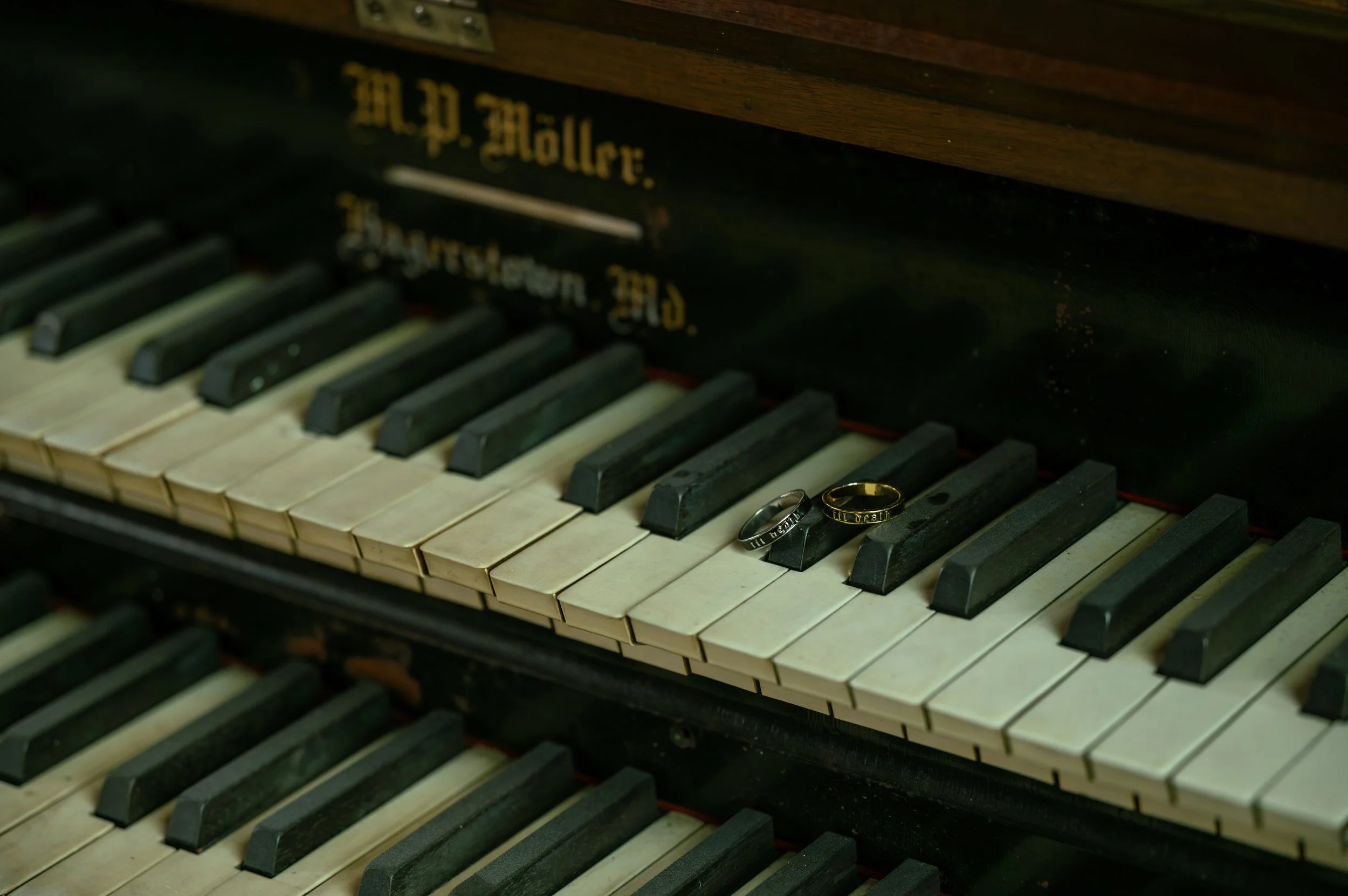 Close-up of an old, dusty piano keyboard with two wedding rings resting on the keys. engaugment photo