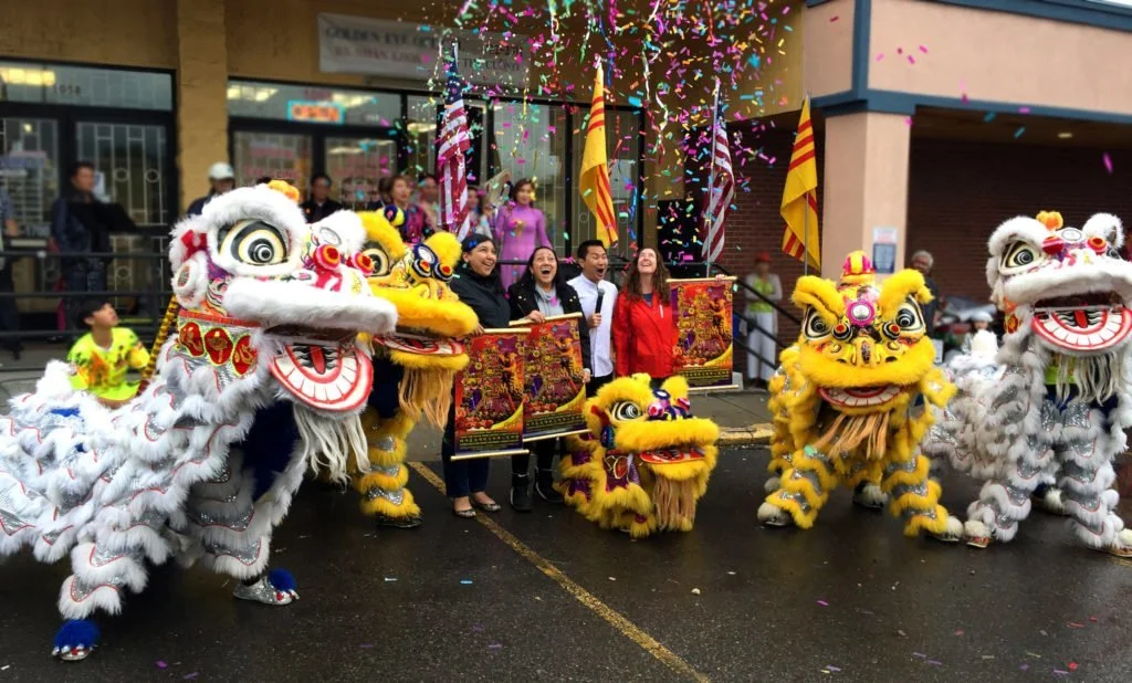 Lion dancers and people holding banners with smiles and happy and surprised faces with confetti above them.