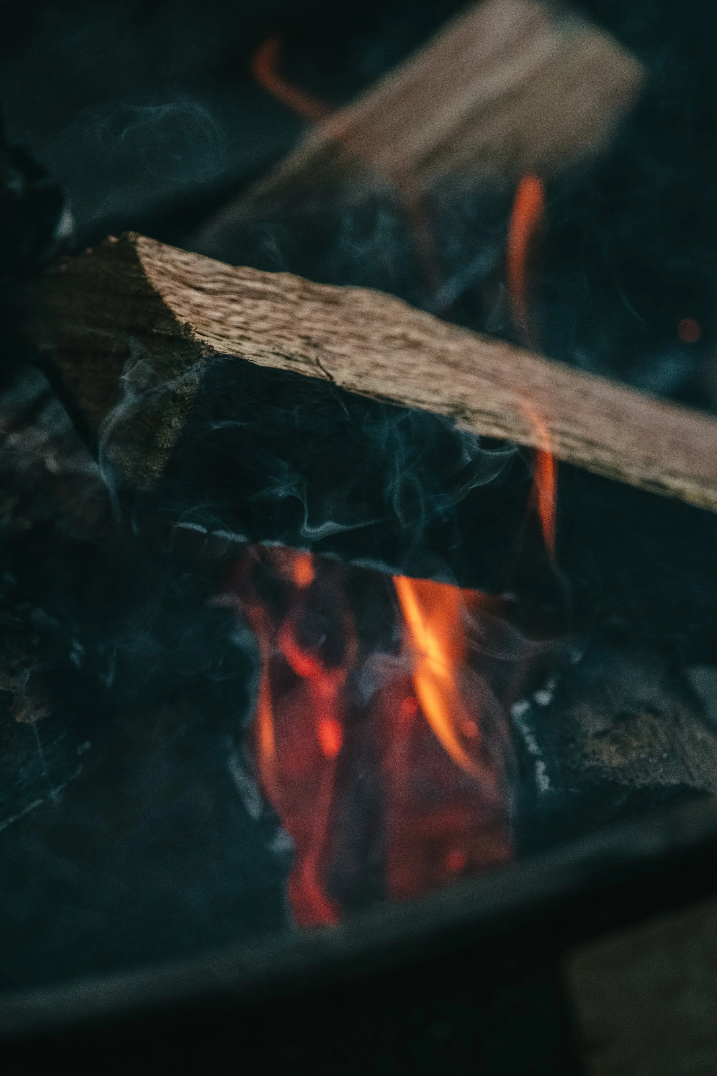 Close-up of a wood fire with orange flames and a piece of wood burning.