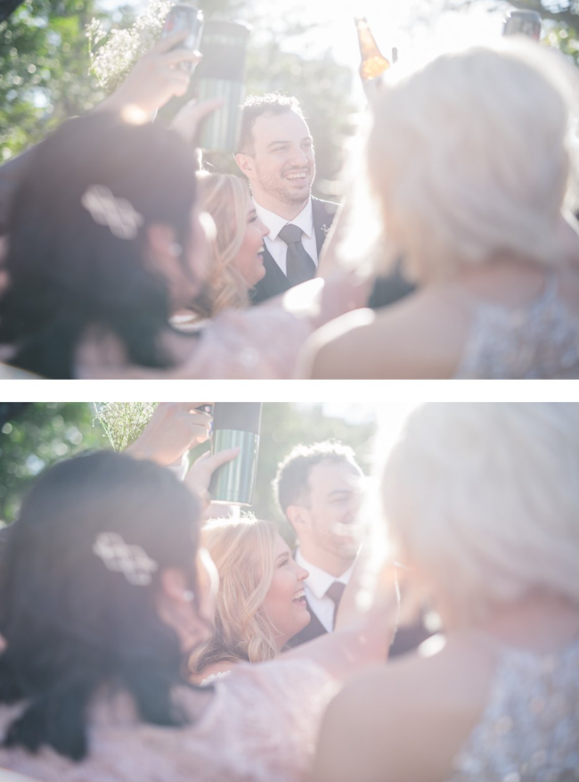A group of people at an outdoor celebration, raising glasses for a toast and smiling, with sunlight filtering through trees in the background.