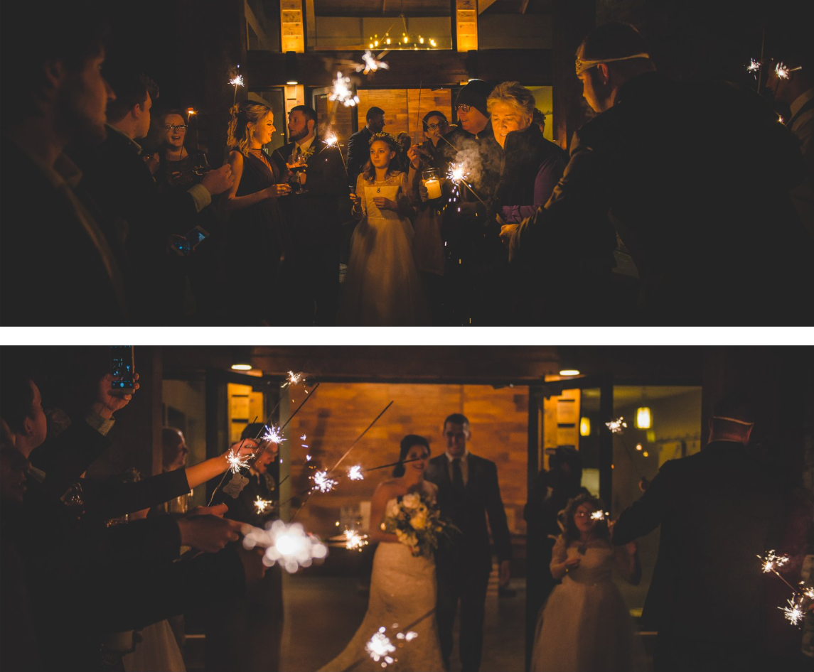 Guests celebrating at a wedding reception holding sparklers, with a bride holding a bouquet and a groom in the background.