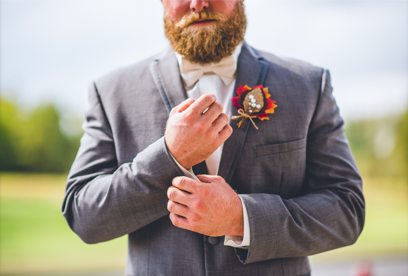 Man in a gray suit with a white bow tie pinning a fall-themed boutonniere on his lapel