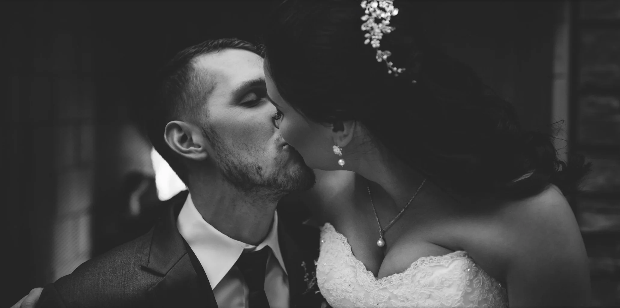 Black and white photograph of a couple kissing, with the woman in a wedding dress and the man in a suit.