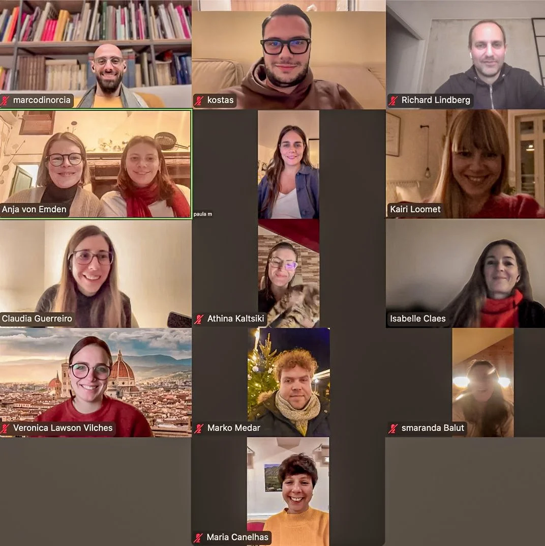 A virtual meeting with 15 participants, each in their own home, smiling and looking at the camera. Some have bookshelves, decorated backgrounds, or festive decorations behind them.