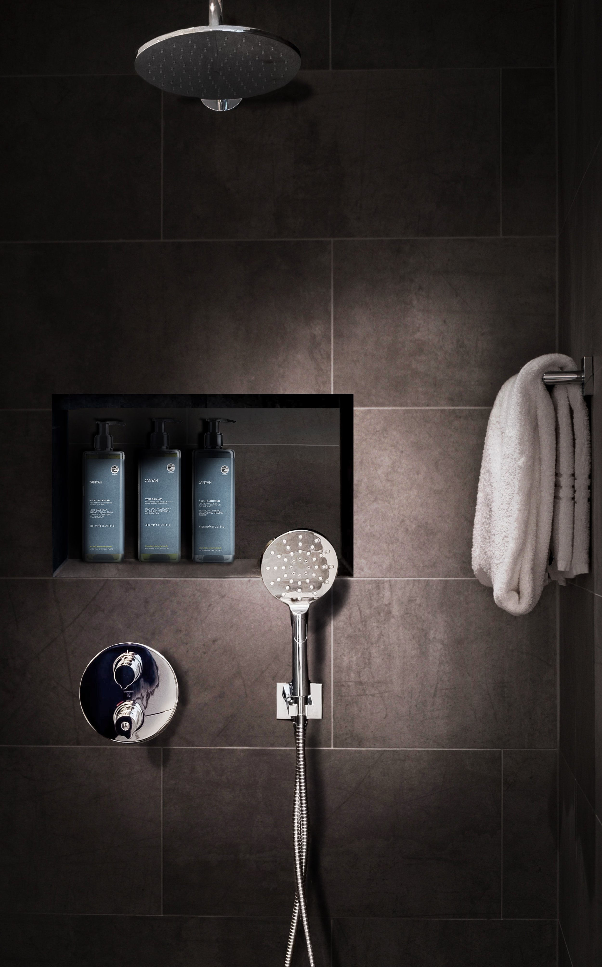 Modern dark-tiled shower with rainfall showerhead, handheld sprayer, toiletries, and hanging towel