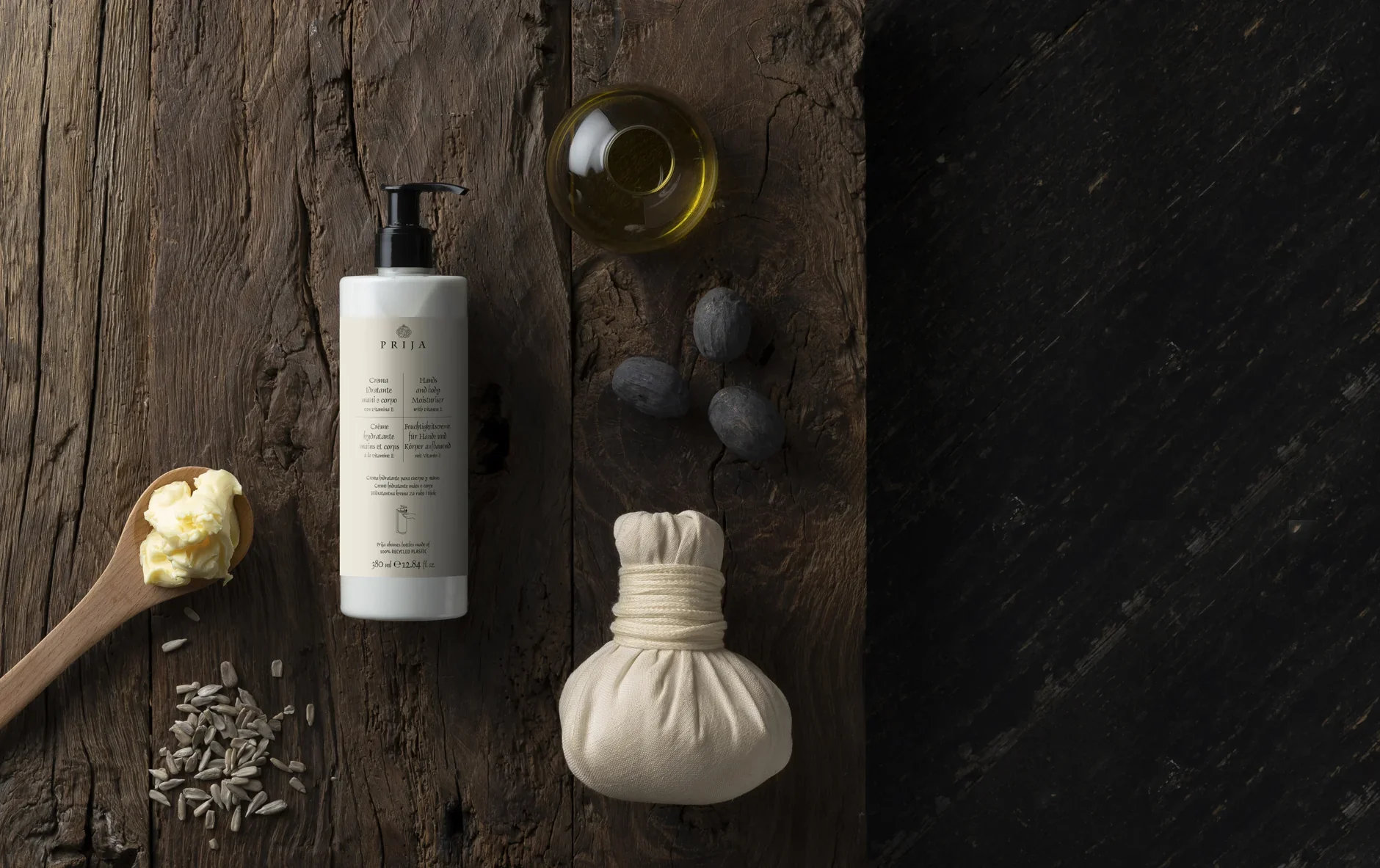 Spa-themed arrangement on rustic wood with a hand and body moisturizer bottle, oil dish, herbal compress, wooden spoon of cream, and seeds.