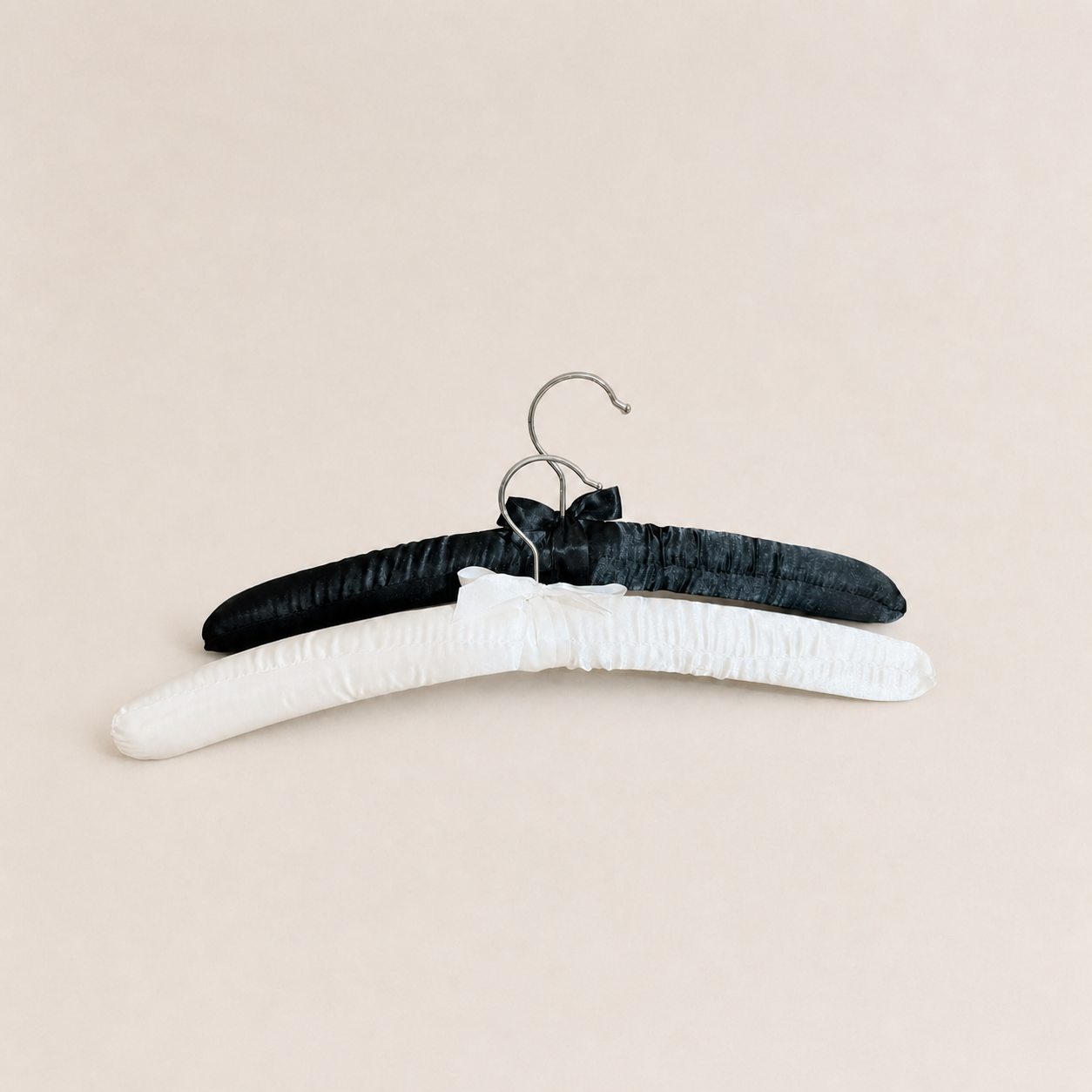 Black and white padded clothes hangers with satin bows on a neutral background