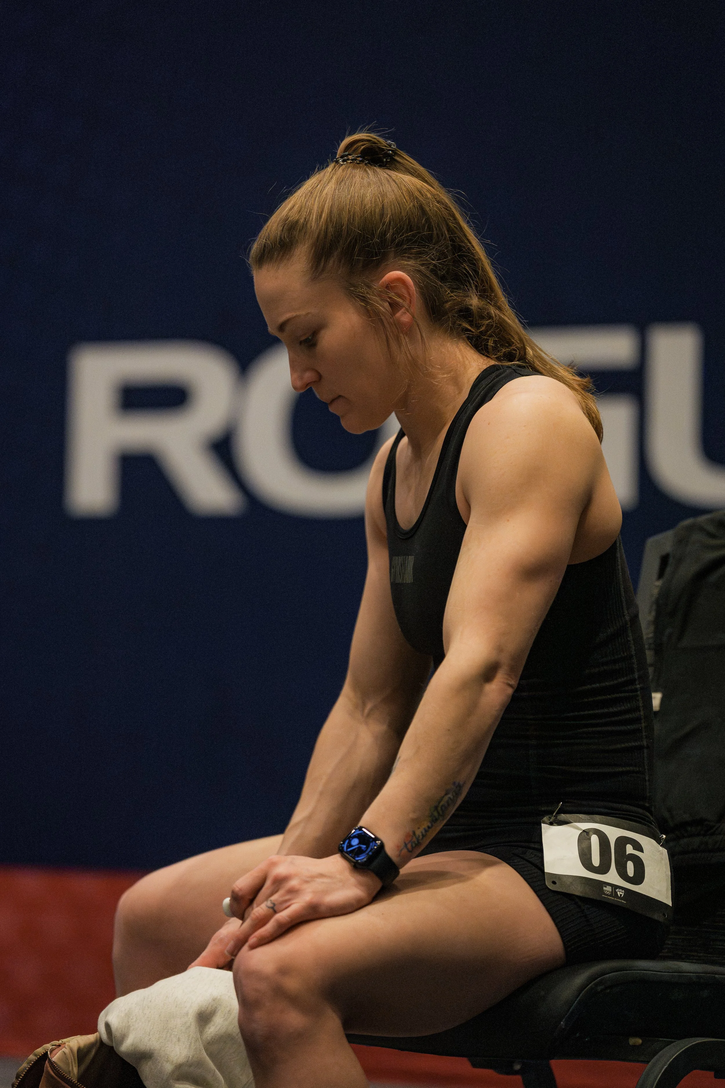 A woman with a ponytail and athletic attire, sitting with her head bowed and hands clasped, in an indoor sports or fitness setting.