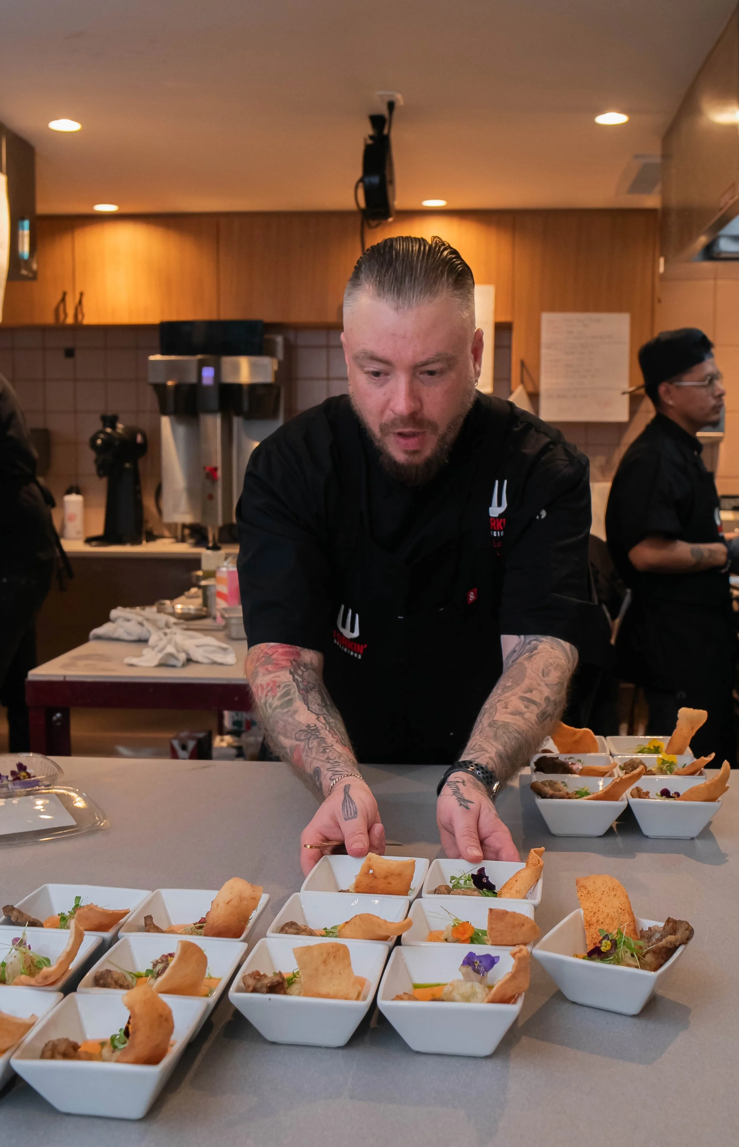Chef arranging small white bowls with gourmet food on kitchen counter.