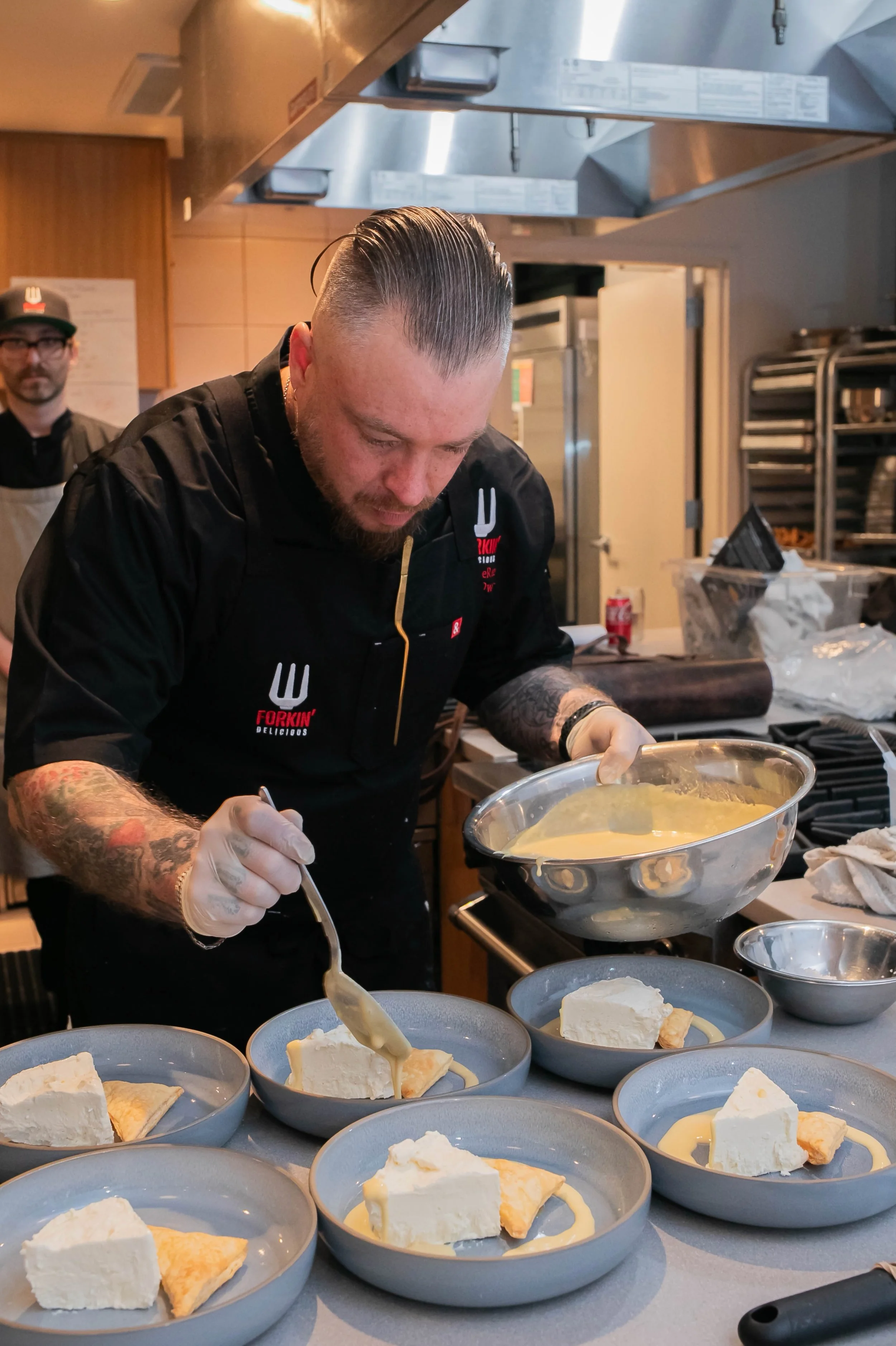 Chef plating desserts with creamy sauce in a commercial kitchen.
