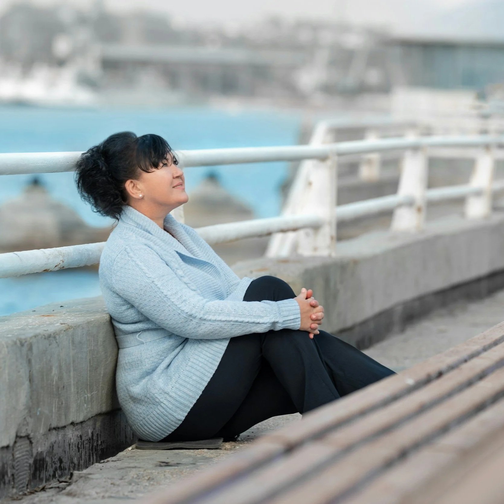 A woman meditating near a body of water with her eyes closed, appearing relaxed.