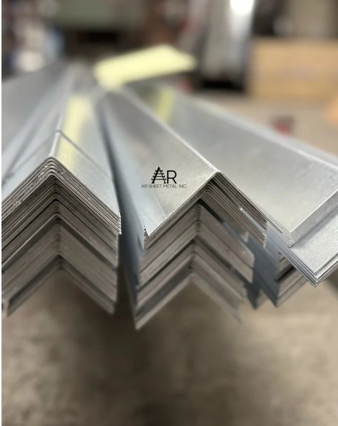 Close-up of stacked metal L-brackets or angles in a workshop or manufacturing setting.