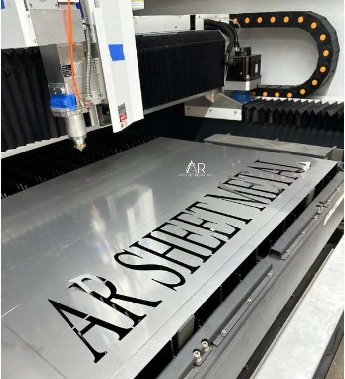 A laser engraving machine cutting the phrase 'AR STREET MEDIA, INC' into a metallic surface.