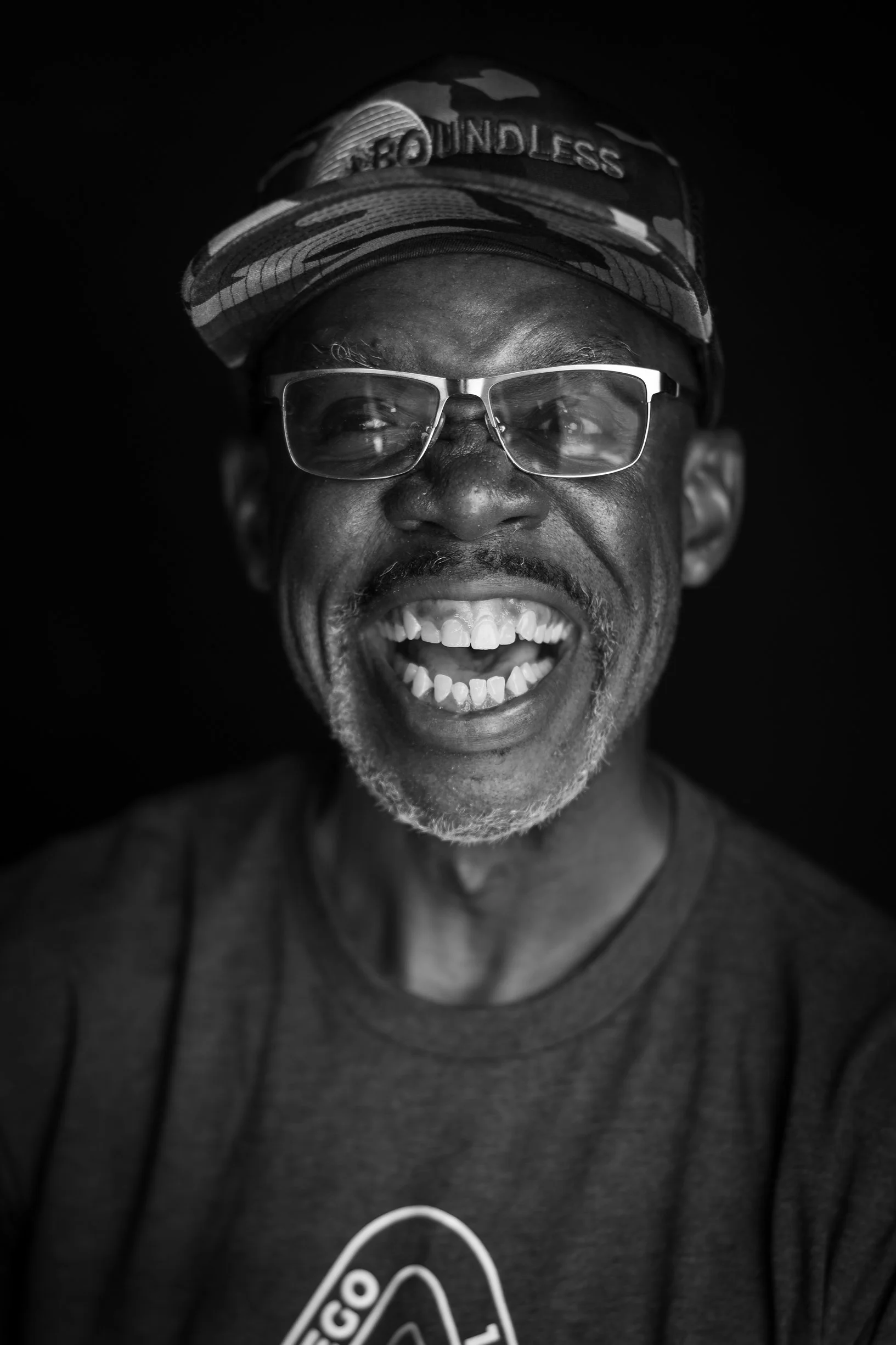 Portrait of a smiling man wearing glasses and a baseball cap.