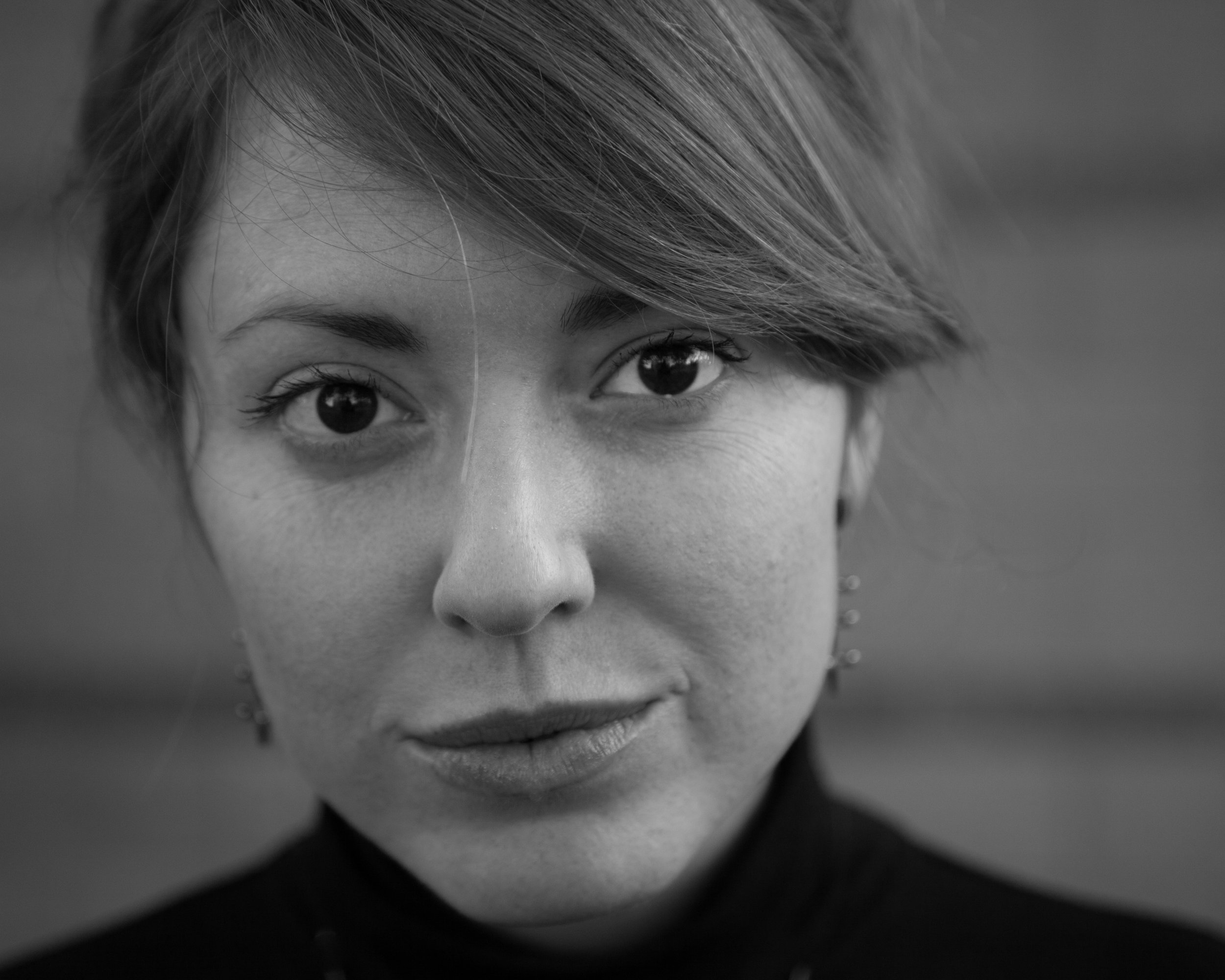 Close-up black and white portrait of a woman with short hair and earrings, looking directly at the camera.
