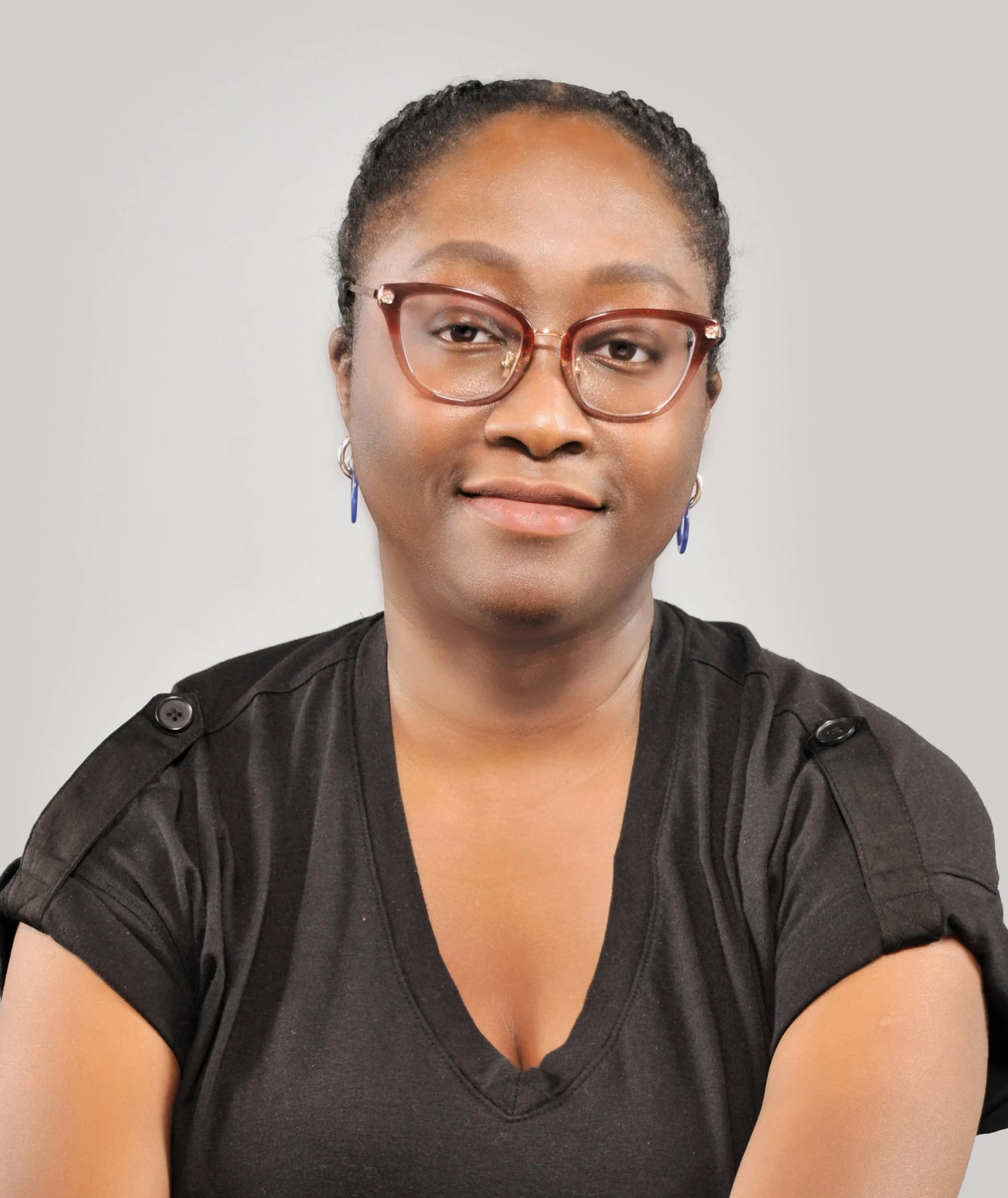 Portrait of a woman with glasses and earrings, wearing a black top, against a plain background.