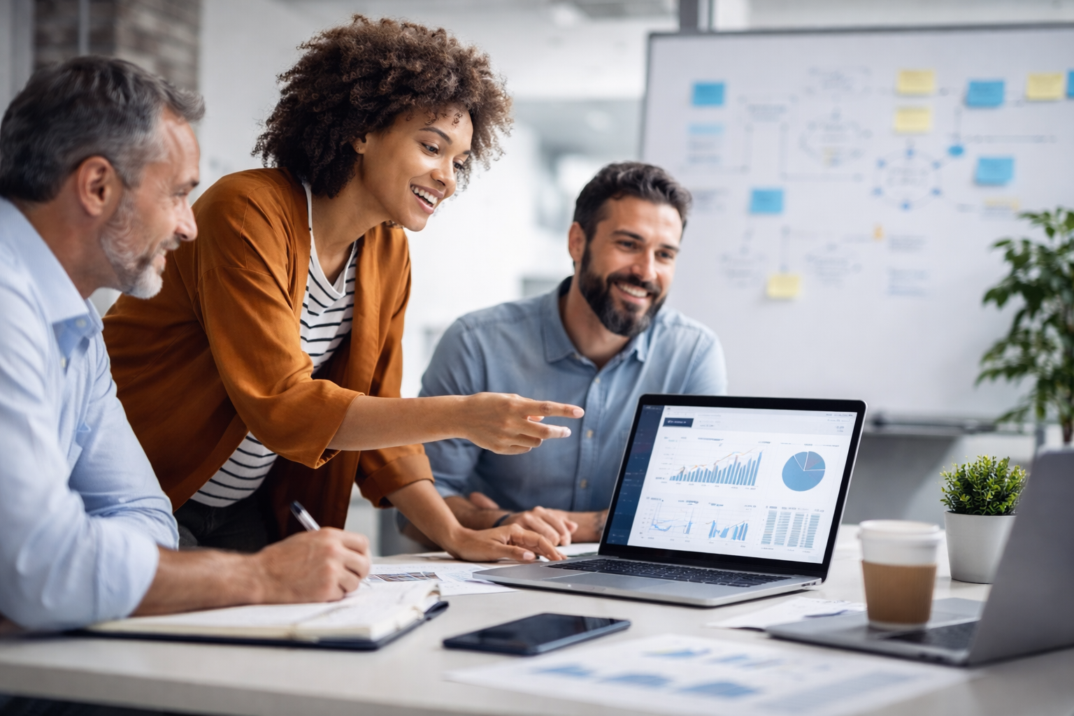 Three professionals reviewing data and graphs on a laptop screen in a modern office, smiling and discussing.
