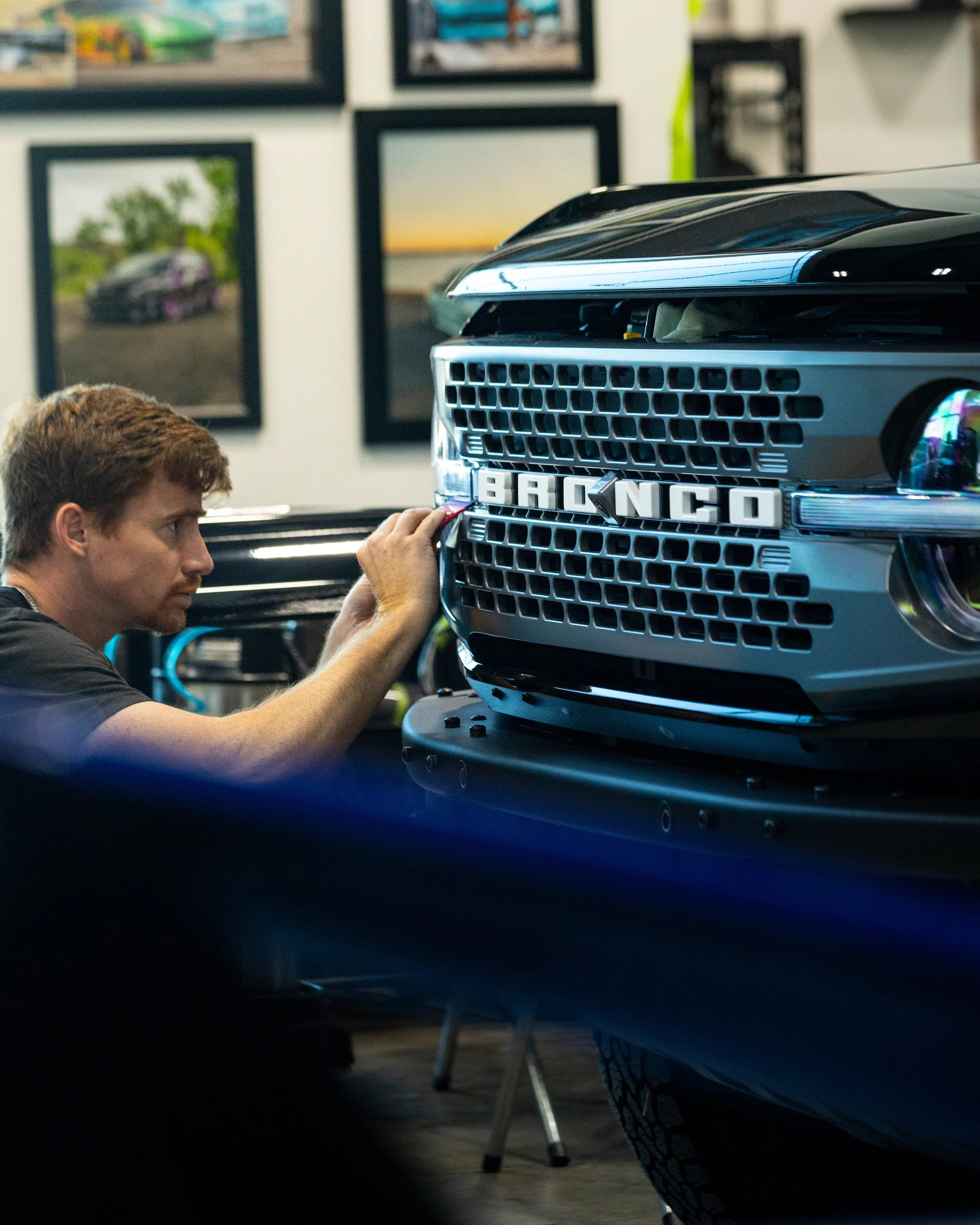 A man working to install PPF on the front grille of a black BRONCO vehicle in a clean indoor garage