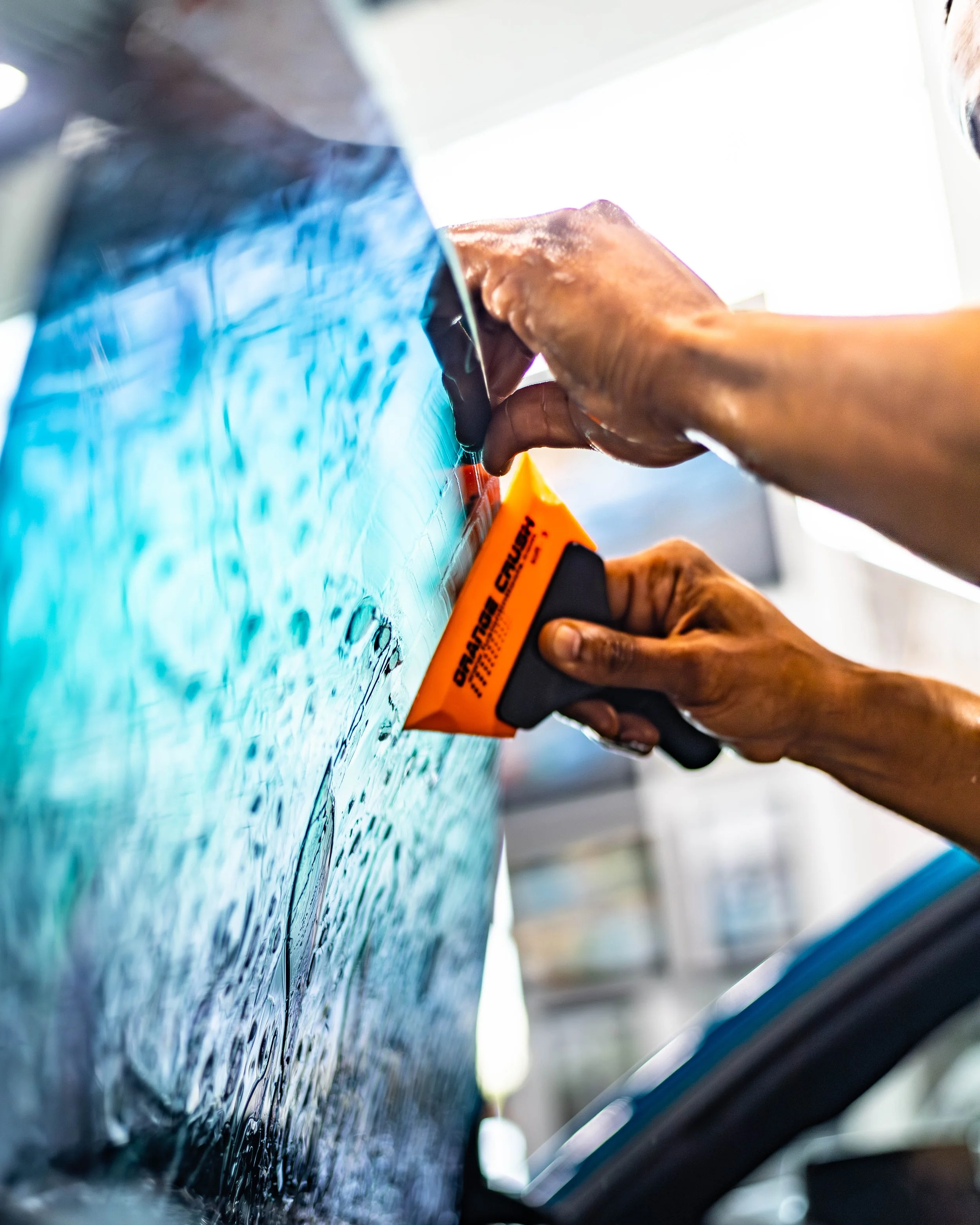 A person installing ceramic window tint a car window with a squeegee.