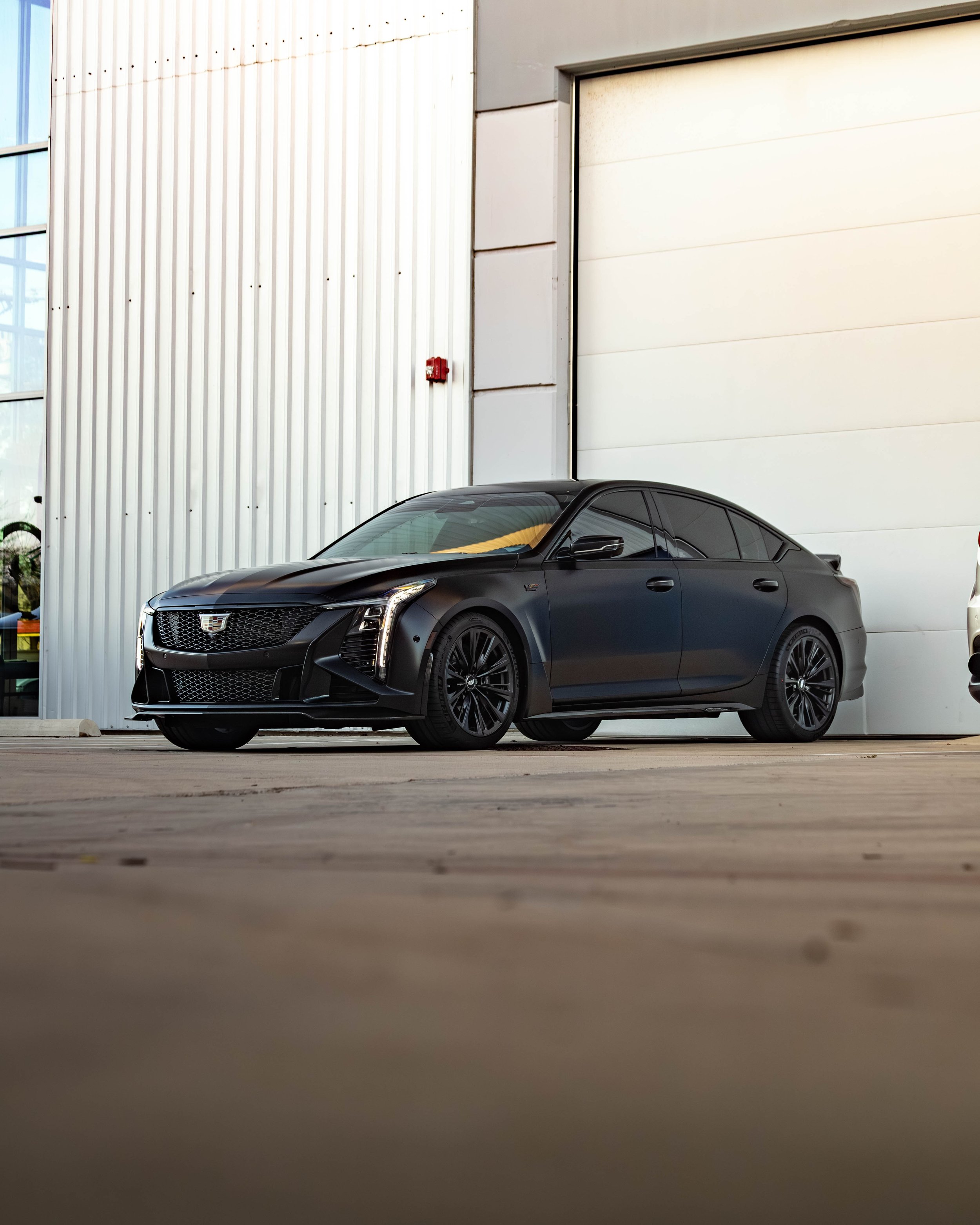 Black luxury sedan parked outside near a large white industrial garage door.