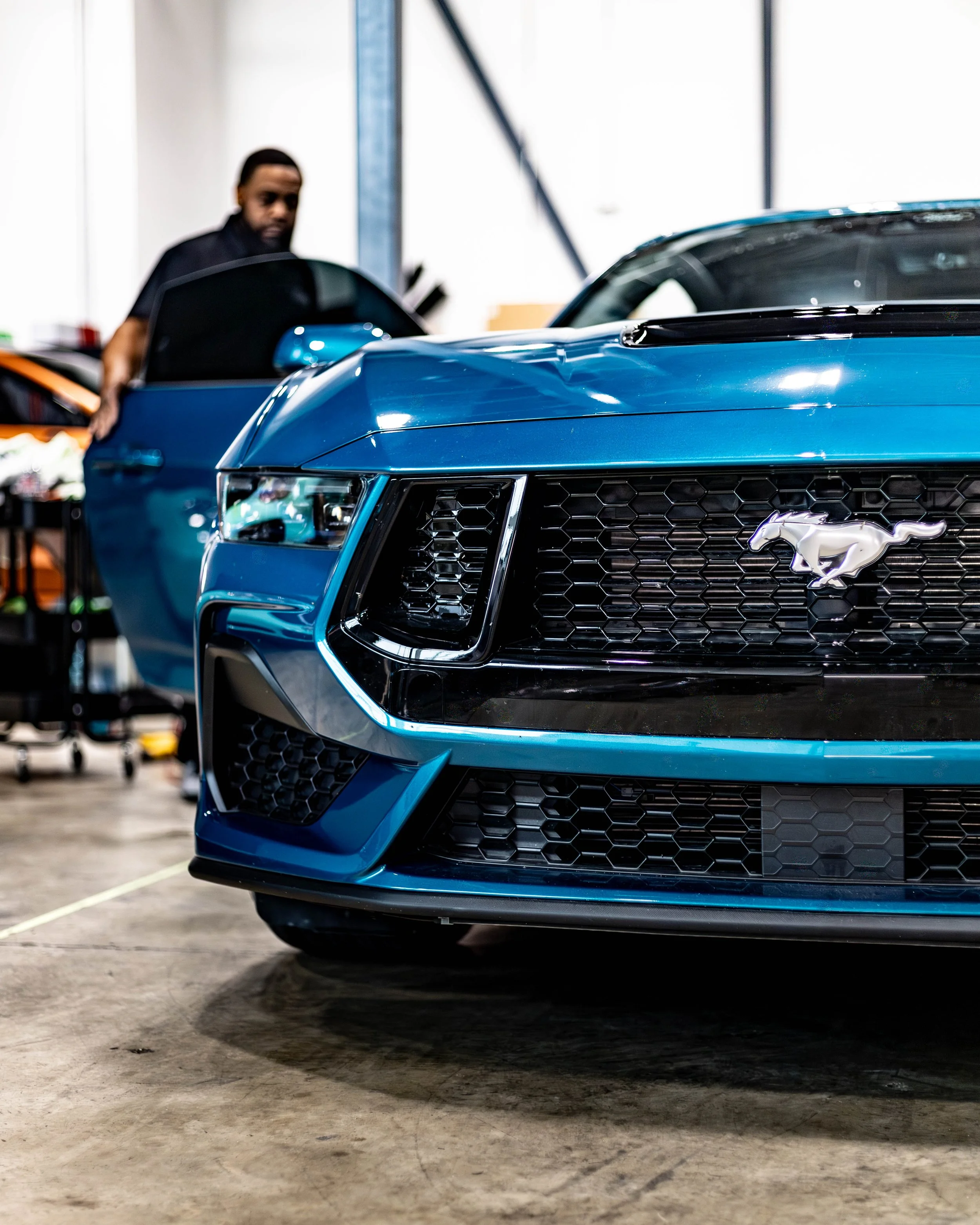 Close-up of a blue Ford Mustang with an employee in the background wrapping up a tint installation