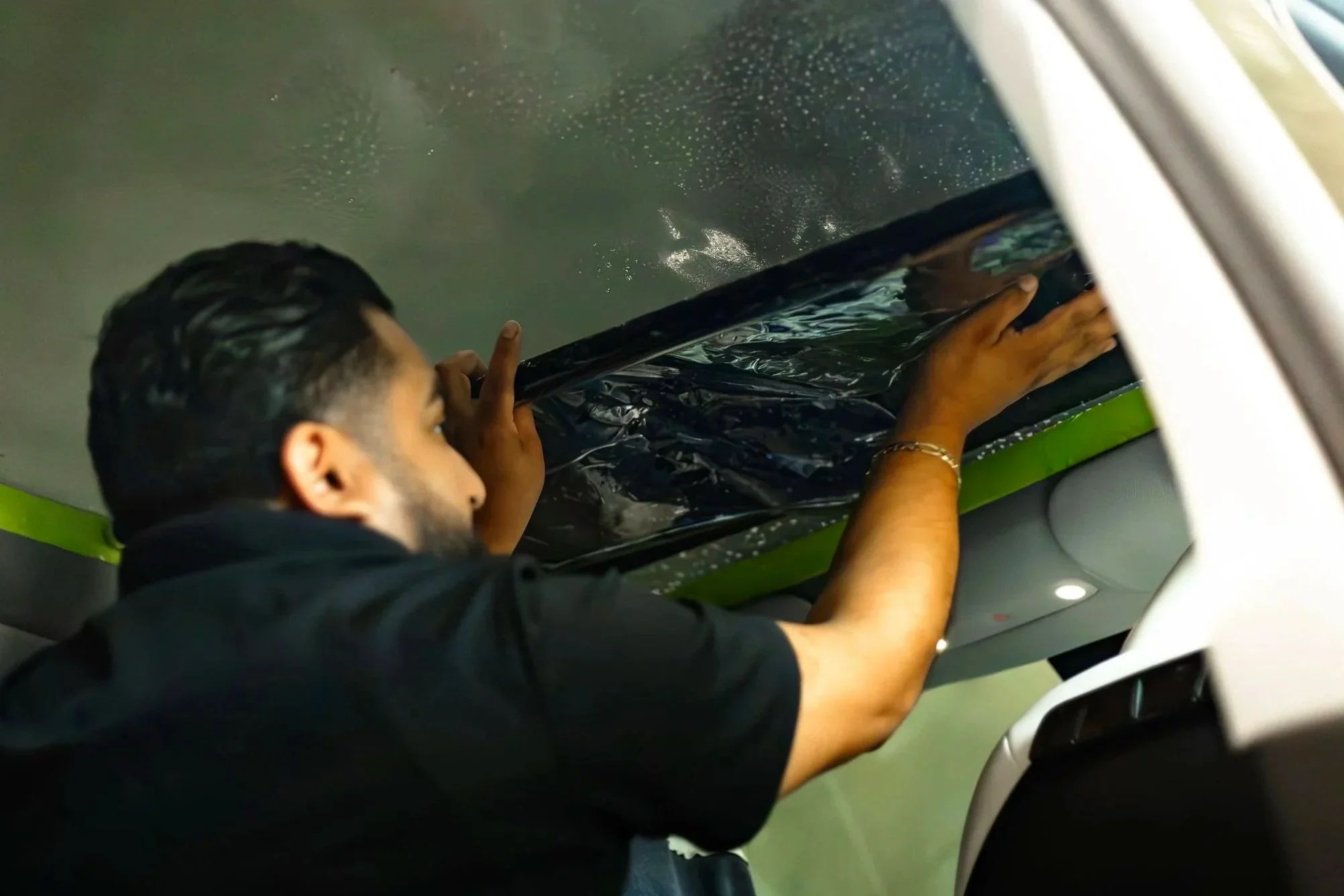 A person installing window tint on the interior panoramic sunroof of a vehicle like a tesla