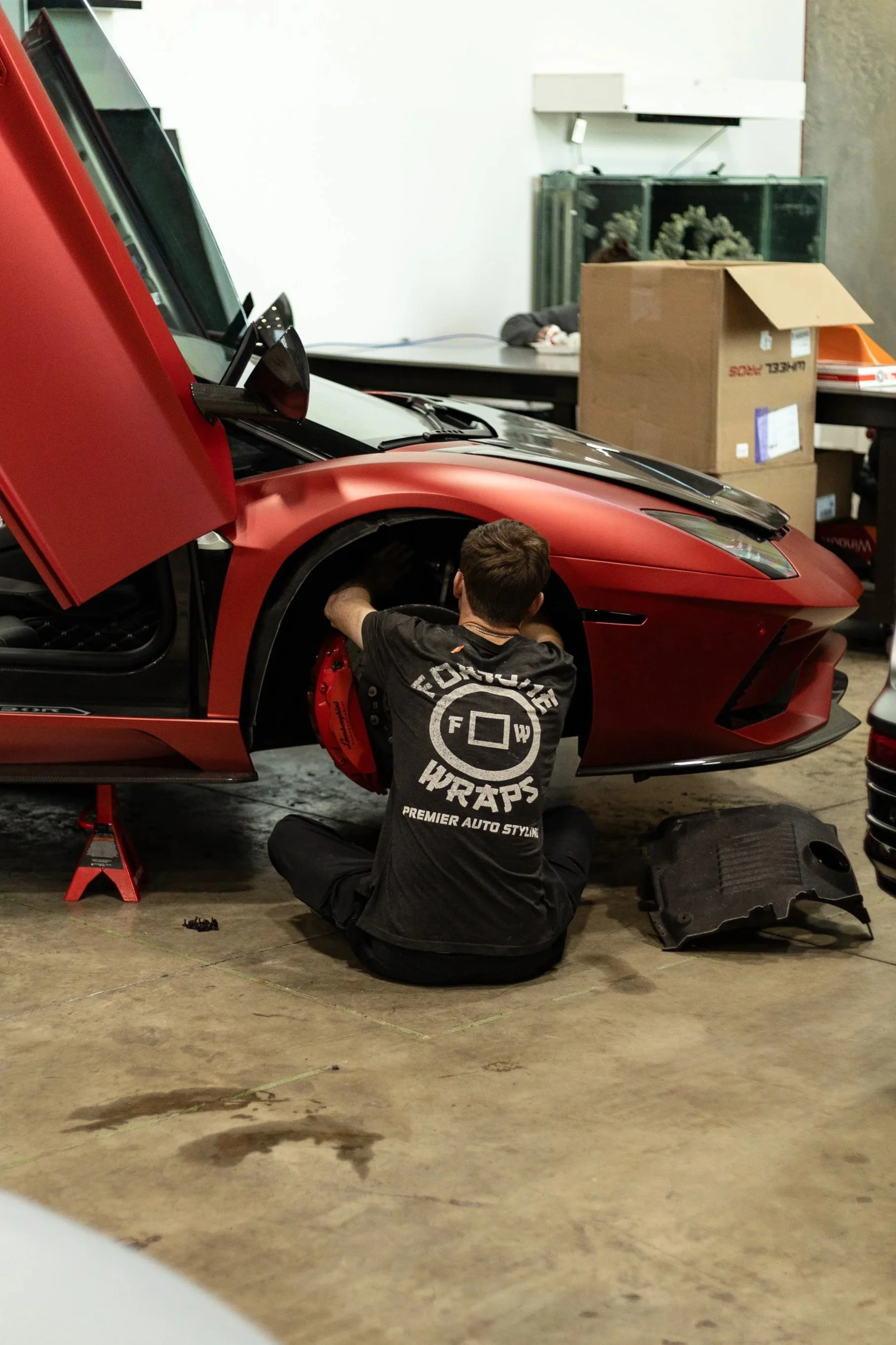 A mechanic (Brian) working on a red sports car (Lamborghini Aventador) inside our garage or workshop. Brian is putting the car back together after the vinyl wrap required a full disassembly to hide that it was originally white.