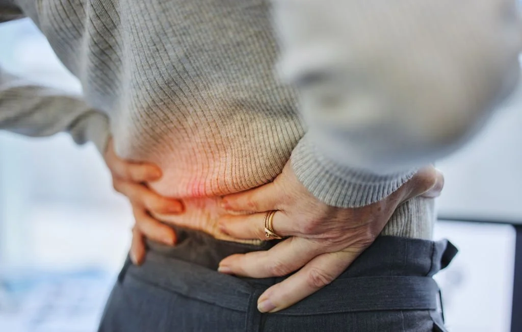 Person holding their lower back due to back pain and stiffness.