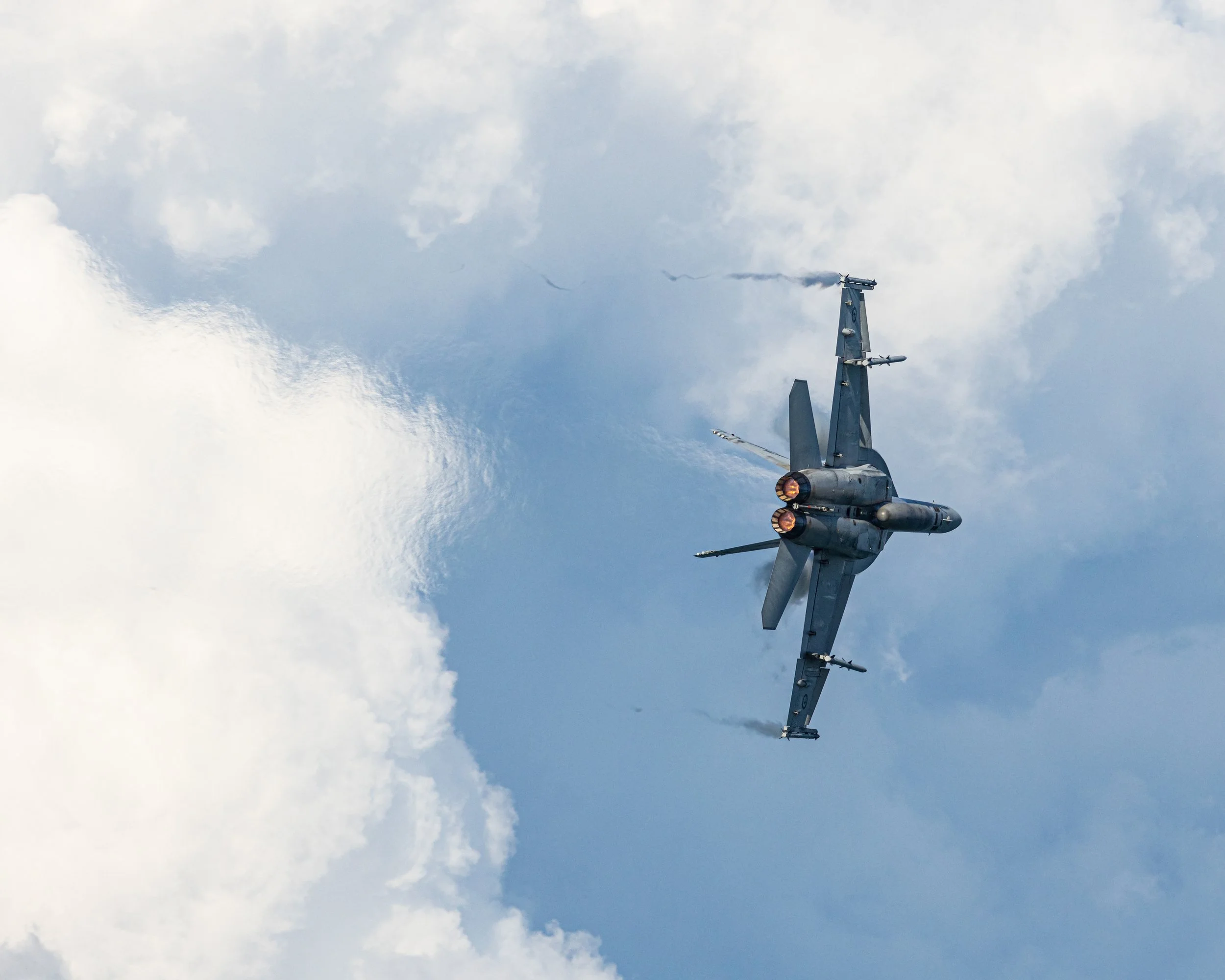 Fighter jet flying in the sky with clouds, with afterburners engaged.
