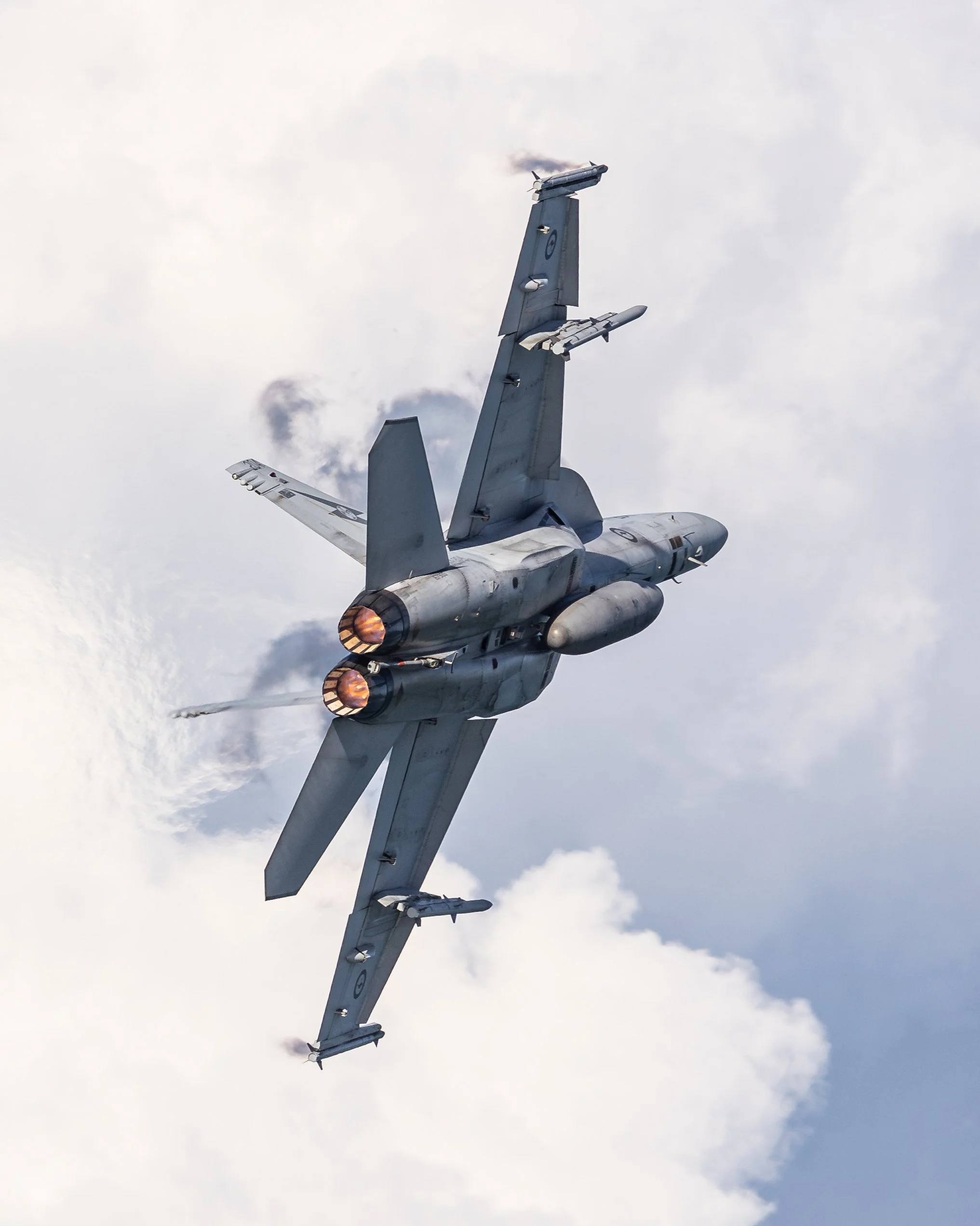 A fighter jet flying upside down with afterburners on against a cloudy sky.