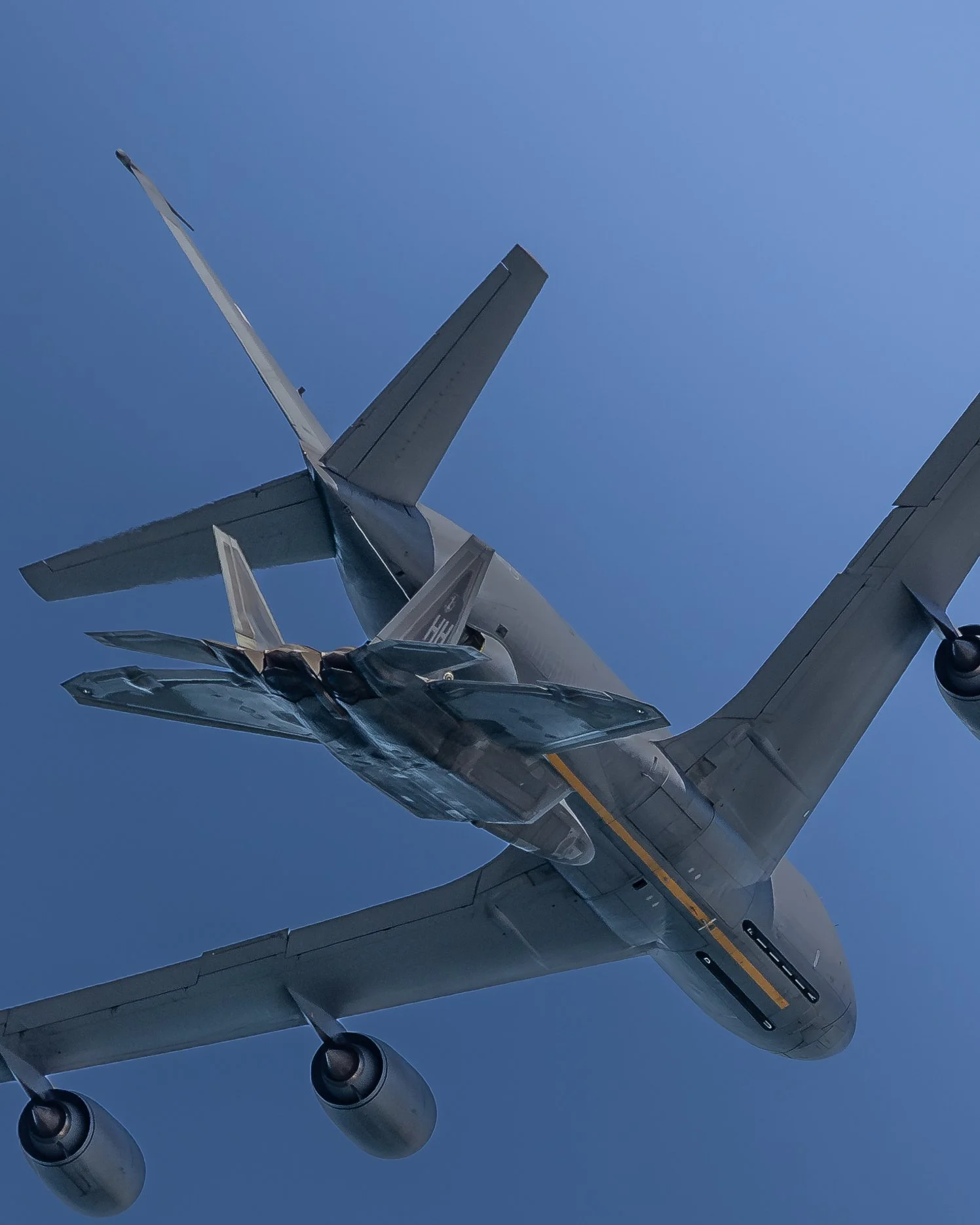 A military fighter jet aircraft flying in clear blue sky, viewed from below.