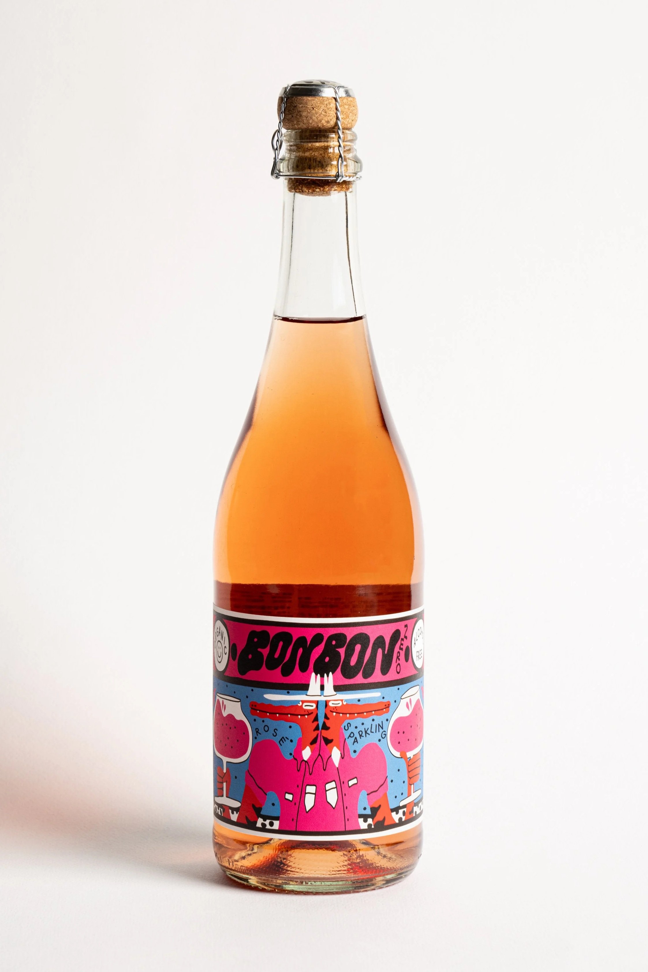 A clear glass bottle with a pink label and cork stopper, containing a pinkish liquid.