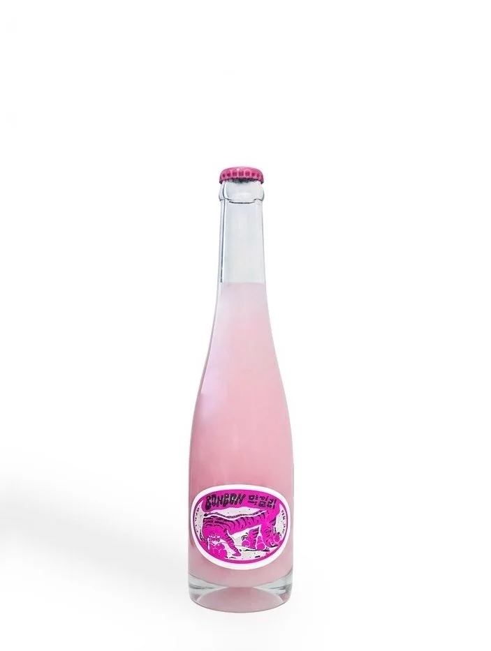 A glass bottle with pink liquid and a pink cap, featuring a label with a pink dinosaur graphic.