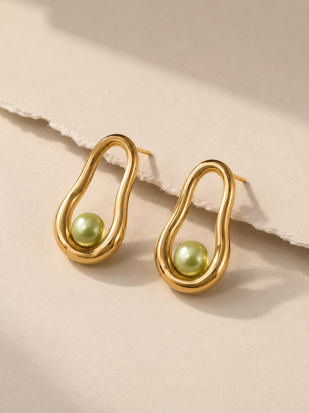 AI campaign visual jewellery  Gold earrings with wavy design and green pearl accents on a beige background.