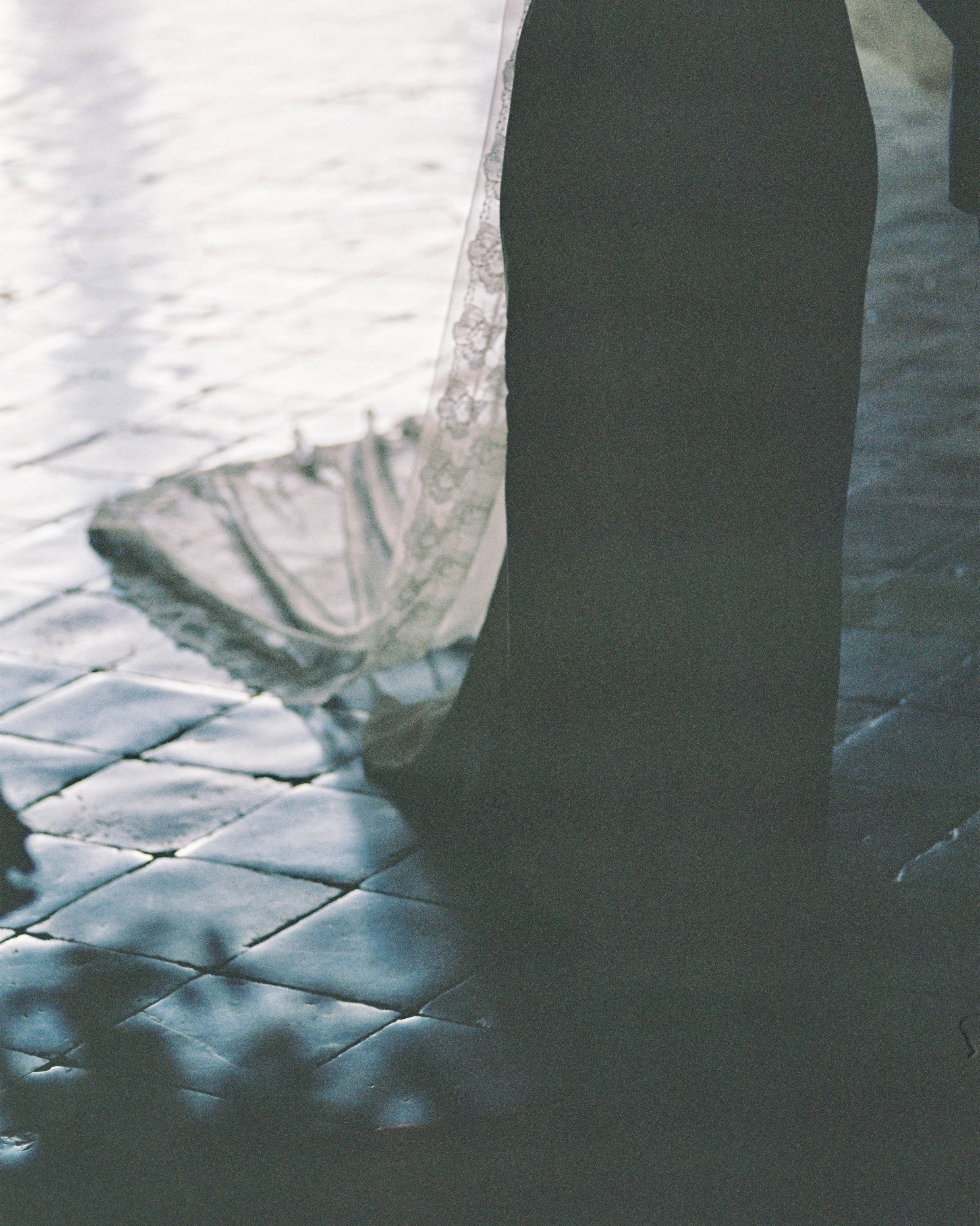 Close-up of a bride's wedding shoe and train on a tiled floor, with water visible in the background.