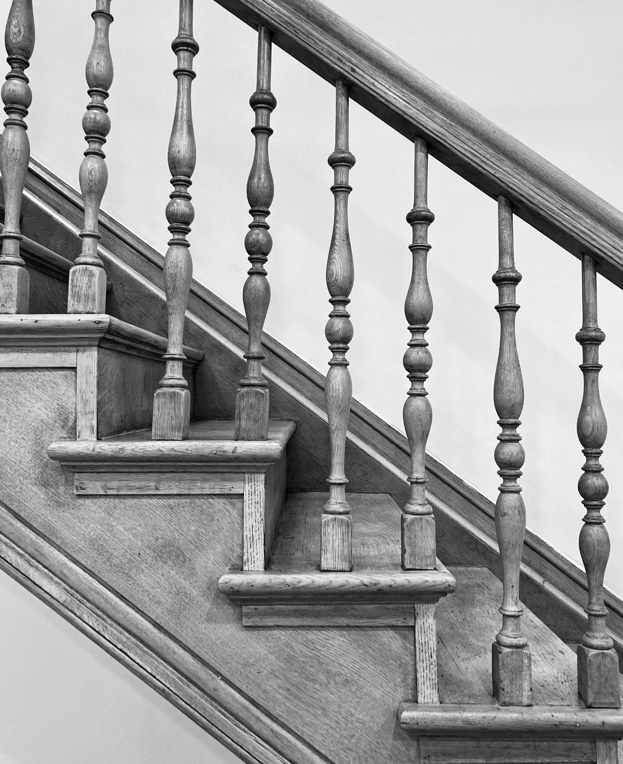 Black and white photo of a wooden staircase with turned balusters and a handrail.