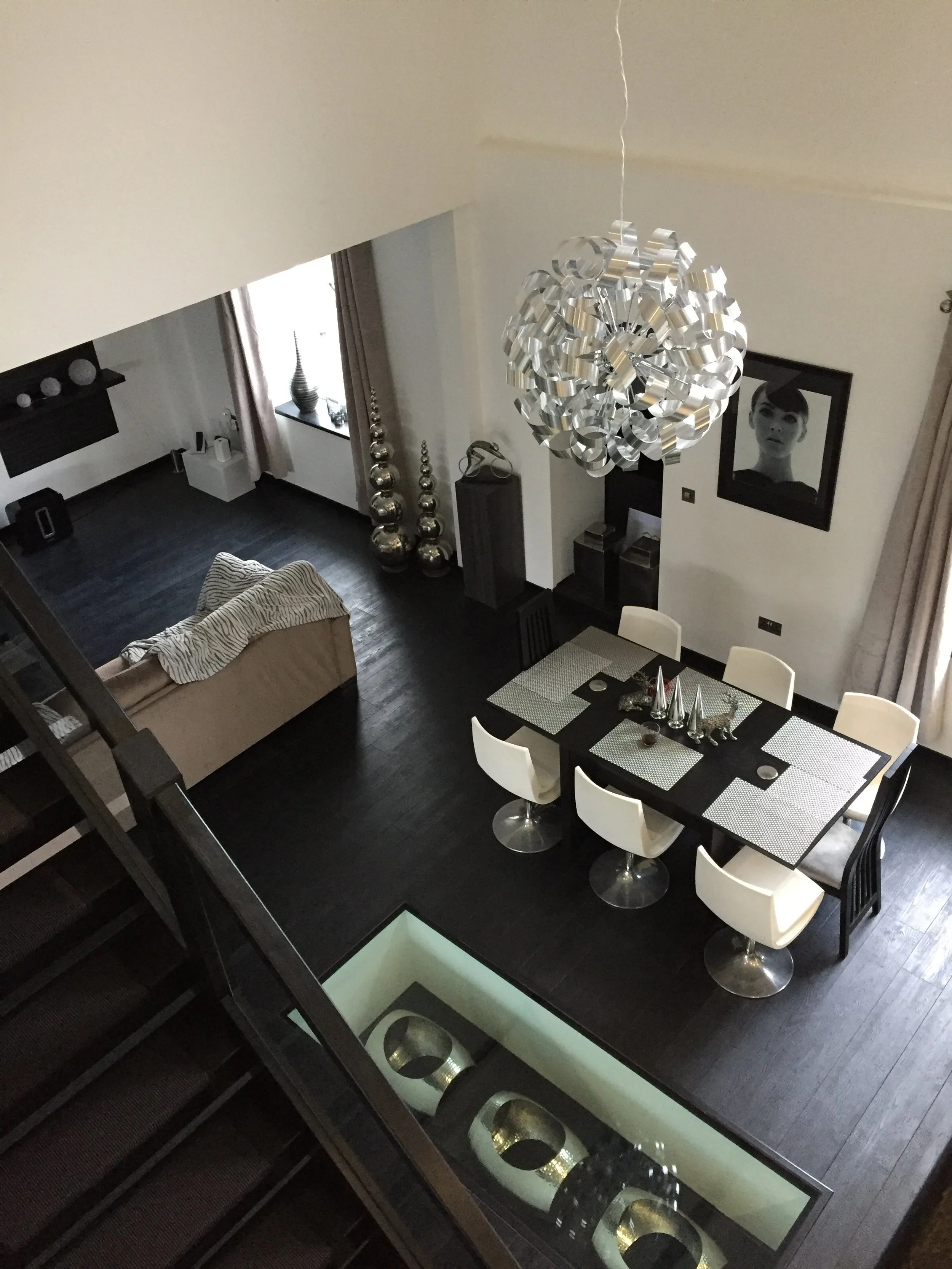 Modern living and dining area with white chairs, glass-top dining table, spiral chandelier, and contemporary decor.